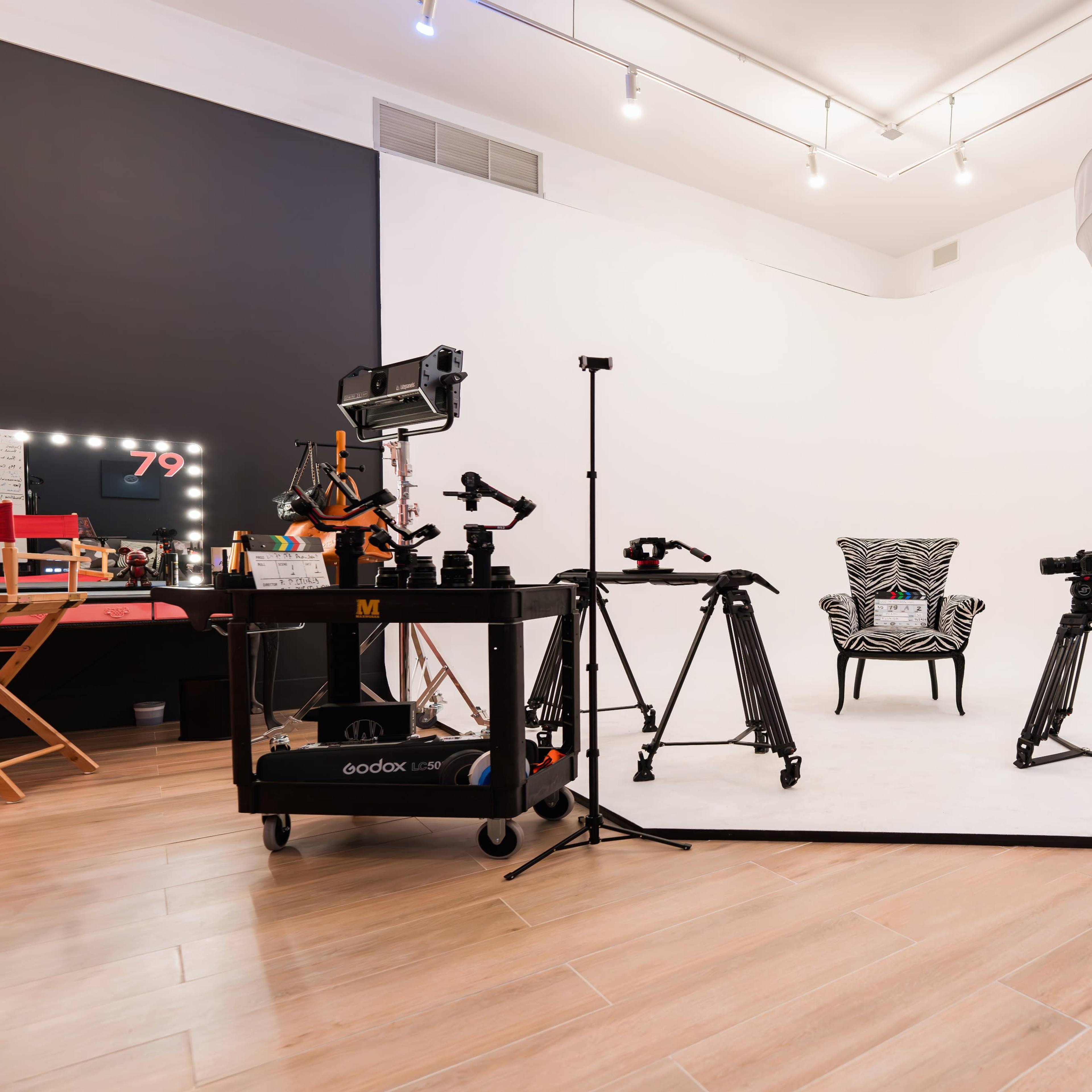 A photography studio features a white backdrop, a zebra-striped chair, and various lighting and camera equipment positioned around the space.