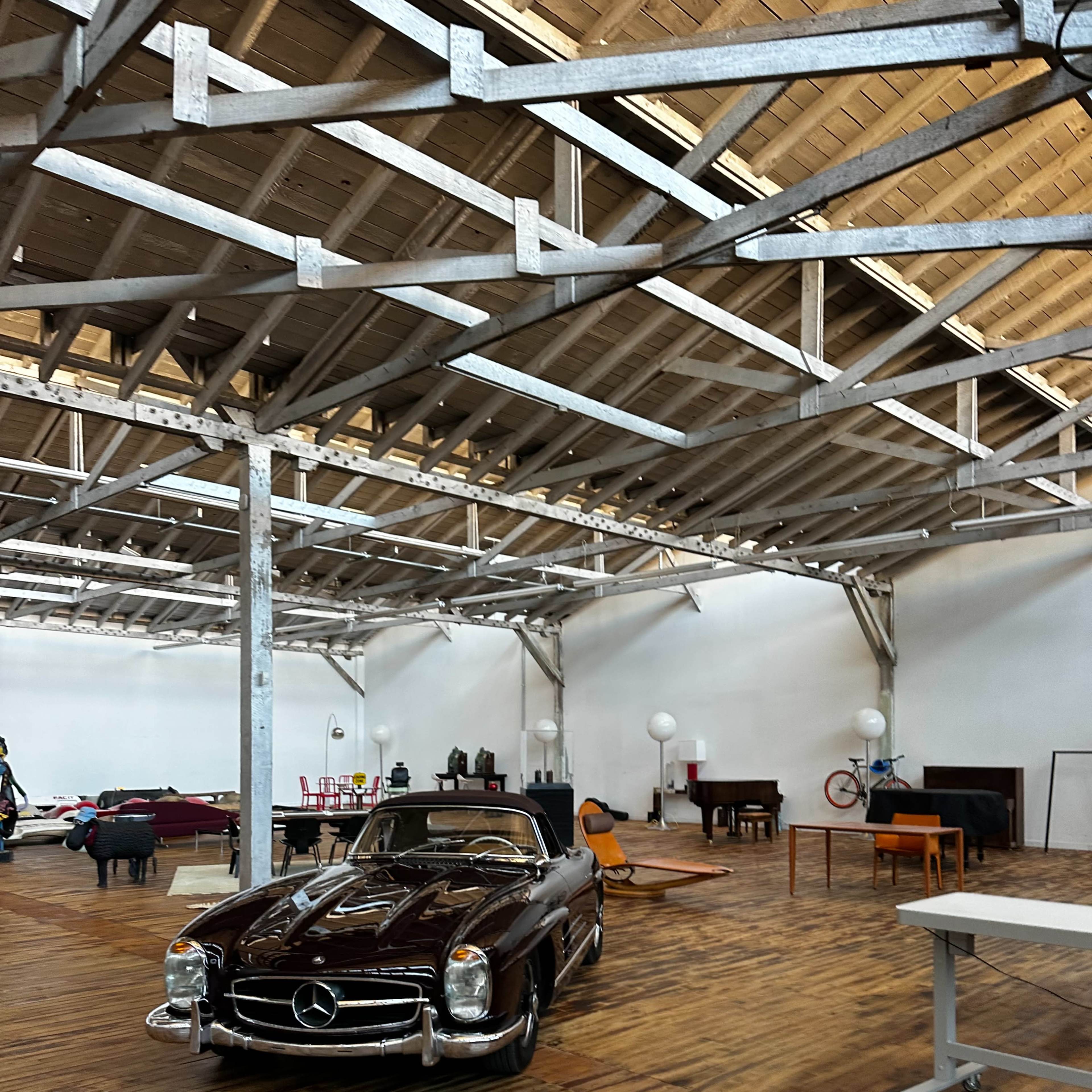A classic Mercedes-Benz sports car is parked in a spacious, modern interior with wooden flooring and exposed beams.