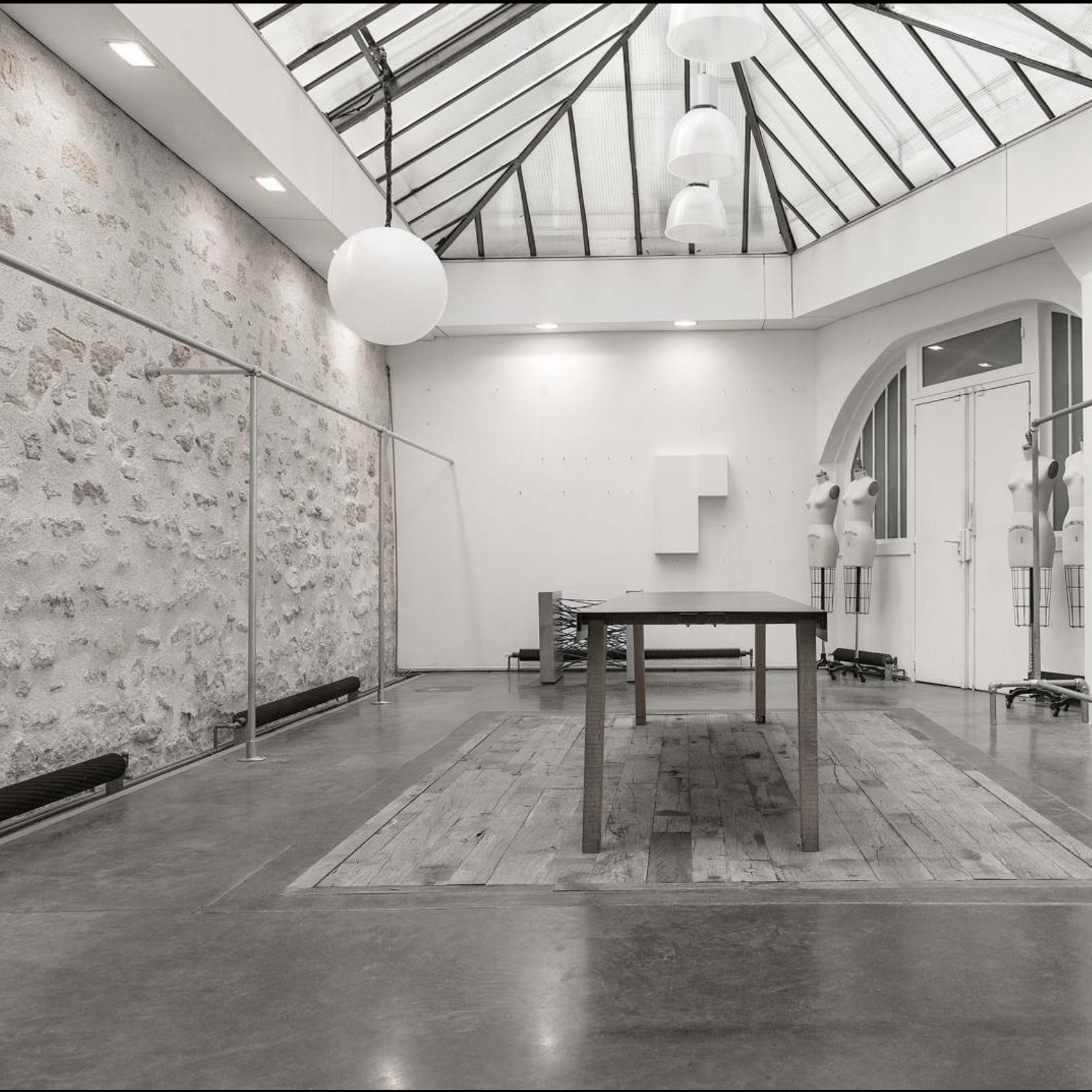 A spacious, well-lit interior with a wooden table in the center, surrounded by a minimalist design featuring a glass ceiling and stone walls.
