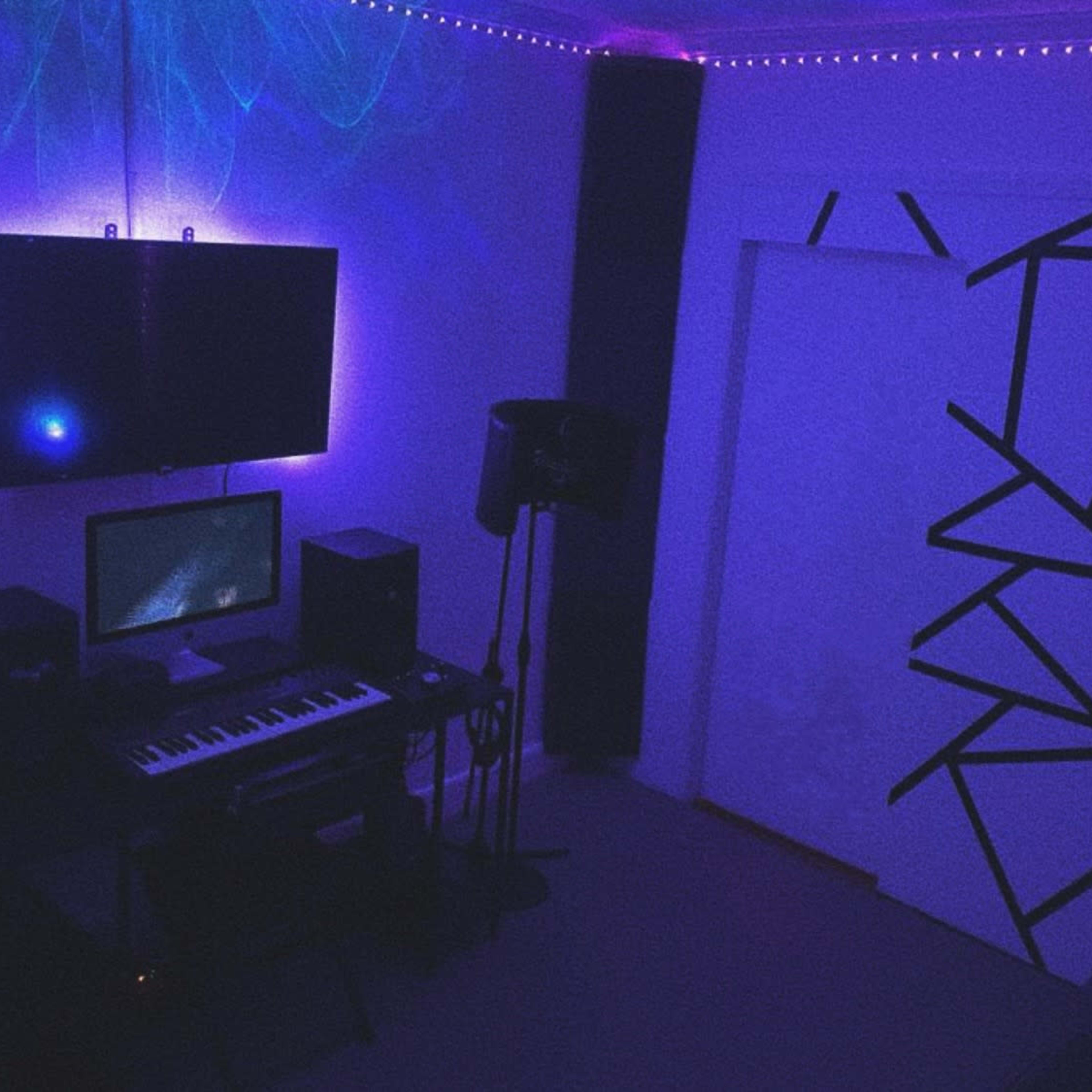 A dimly lit music studio with a keyboard, computer, and monitor set up, surrounded by illuminated walls and a patterned door.