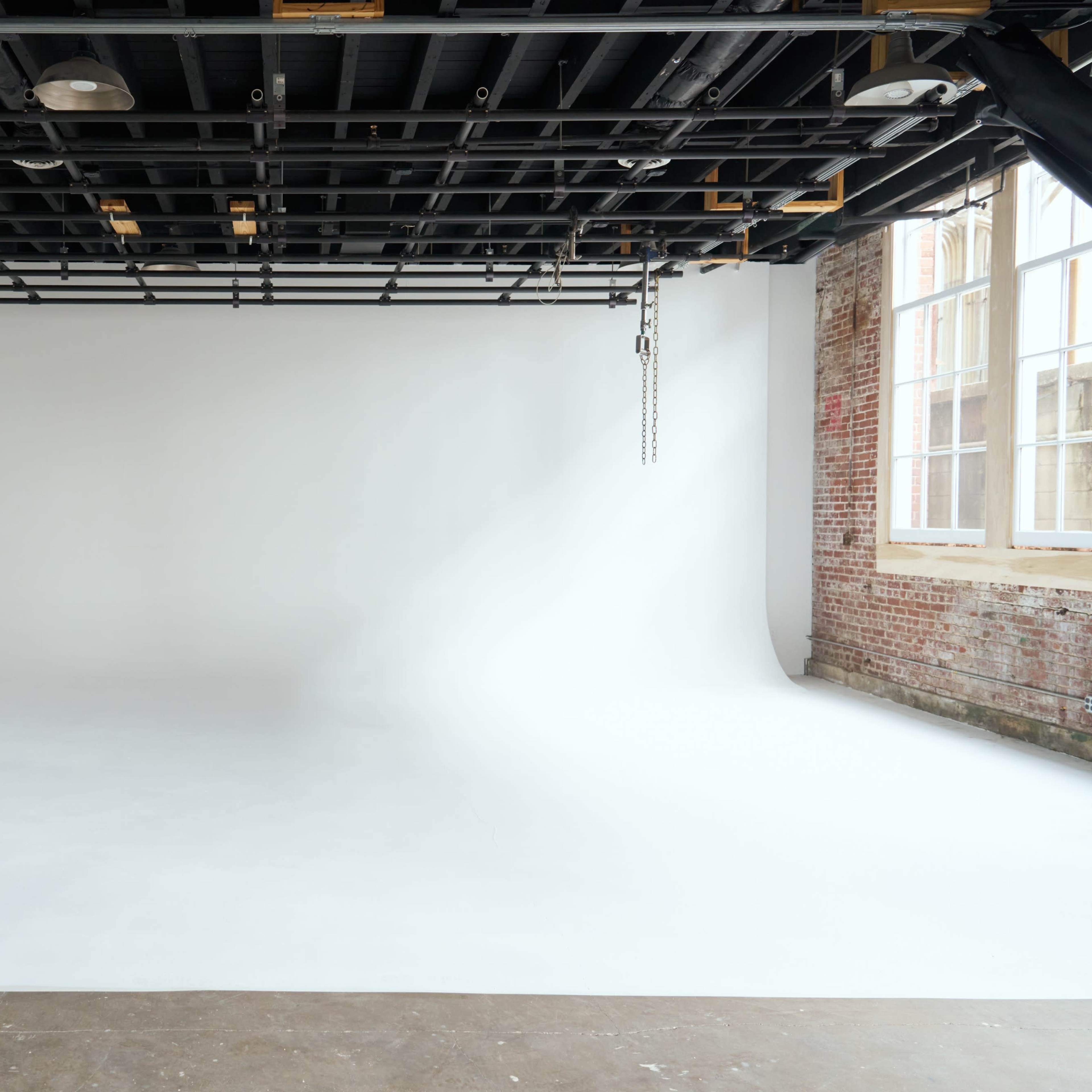 A spacious photography studio with a seamless white background and exposed brick walls.