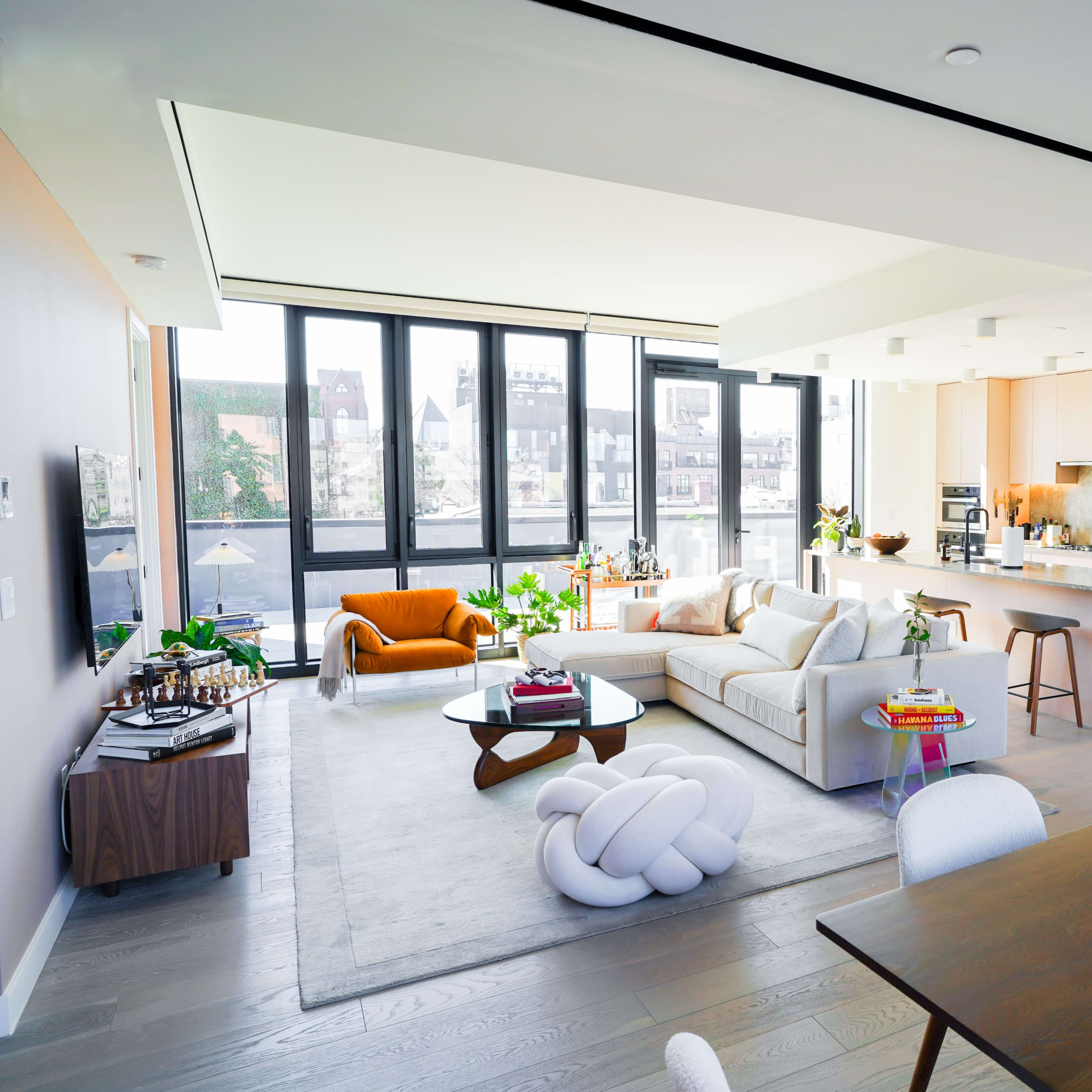 A modern open-concept living space features a kitchen, dining area, and a cozy sitting area with large windows allowing natural light to fill the room.
