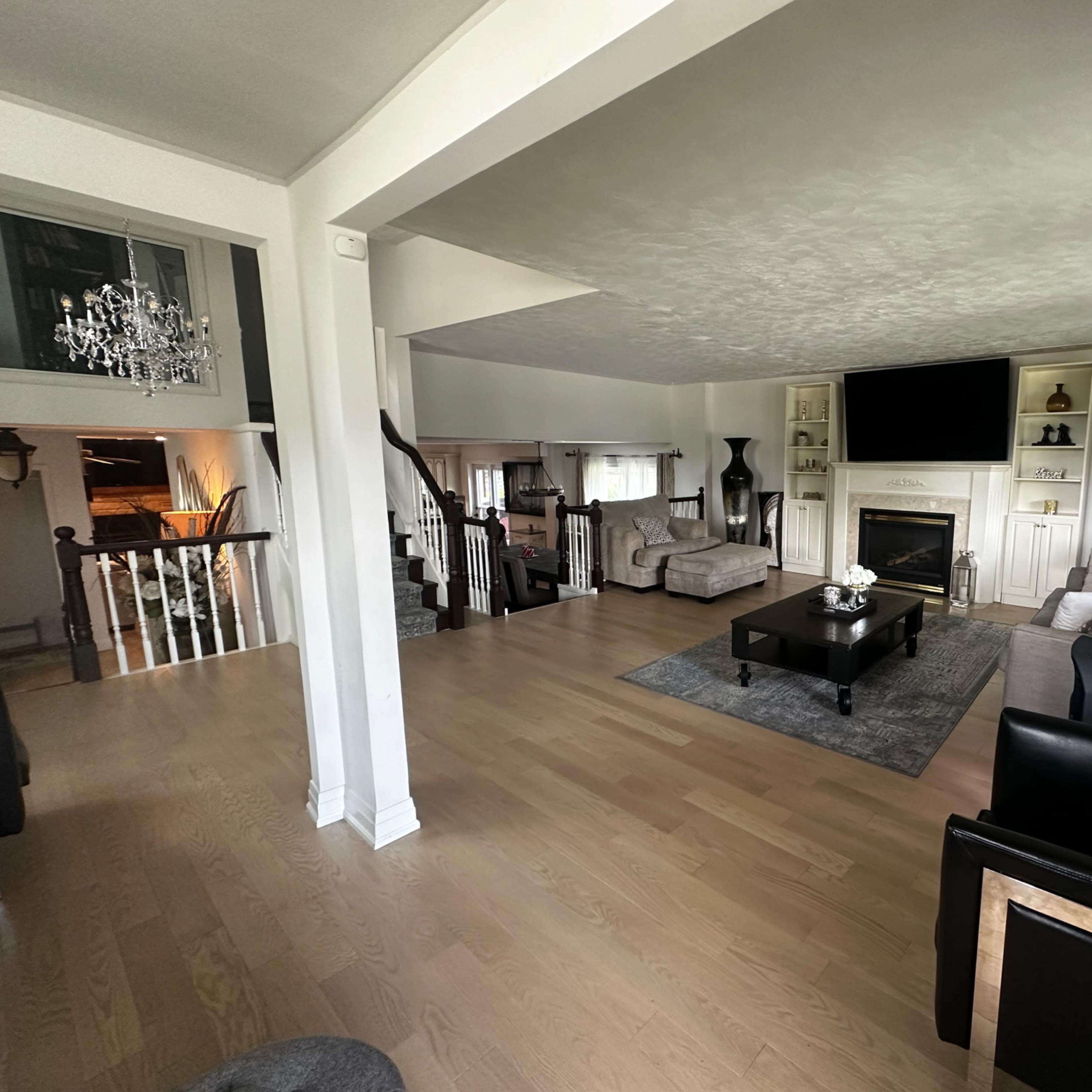 A spacious living room features a fireplace, large television, and comfortable seating arrangements, with wooden floors and decorative elements throughout.