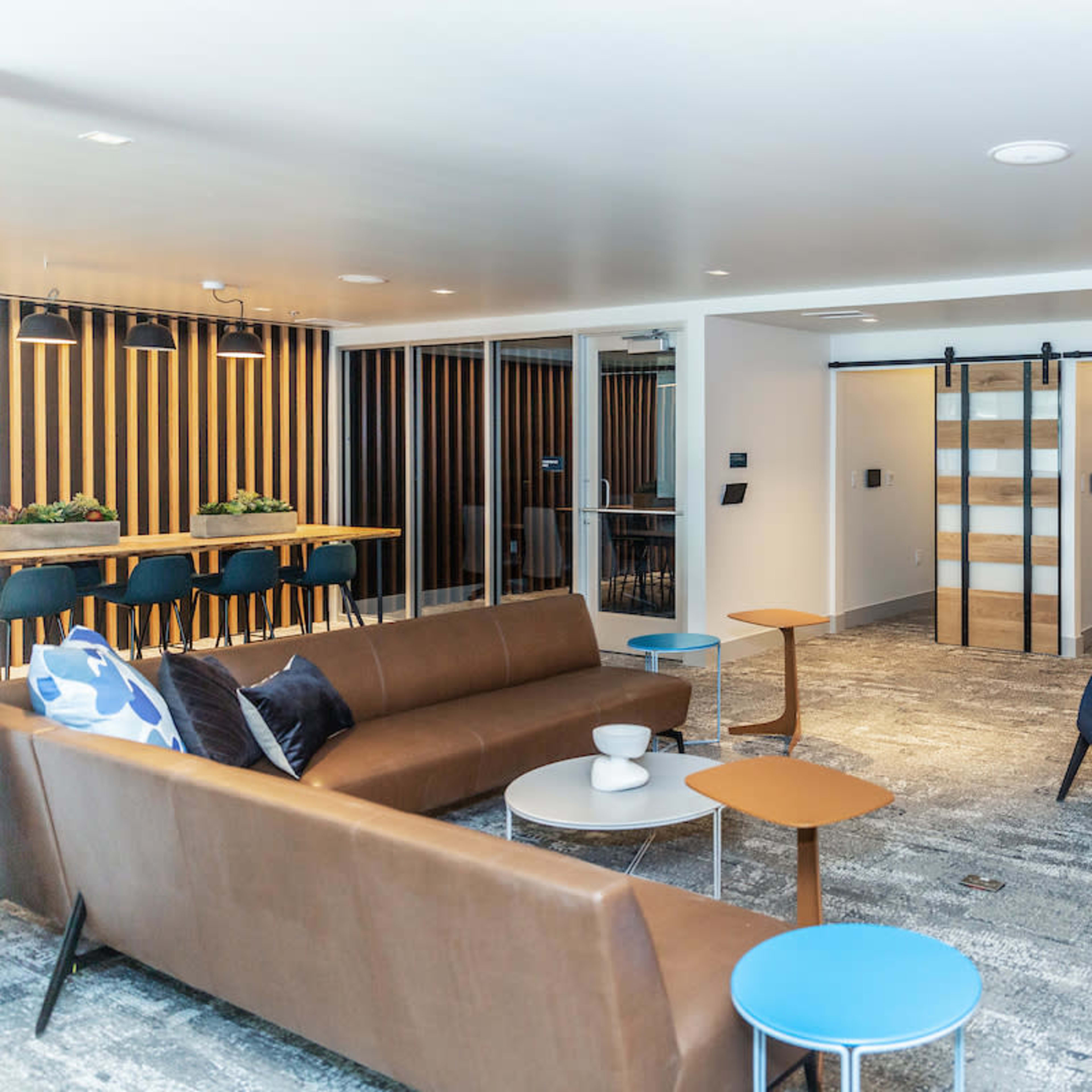 A modern lounge area featuring brown sofas, a blue chair, small tables, and wooden partition walls.