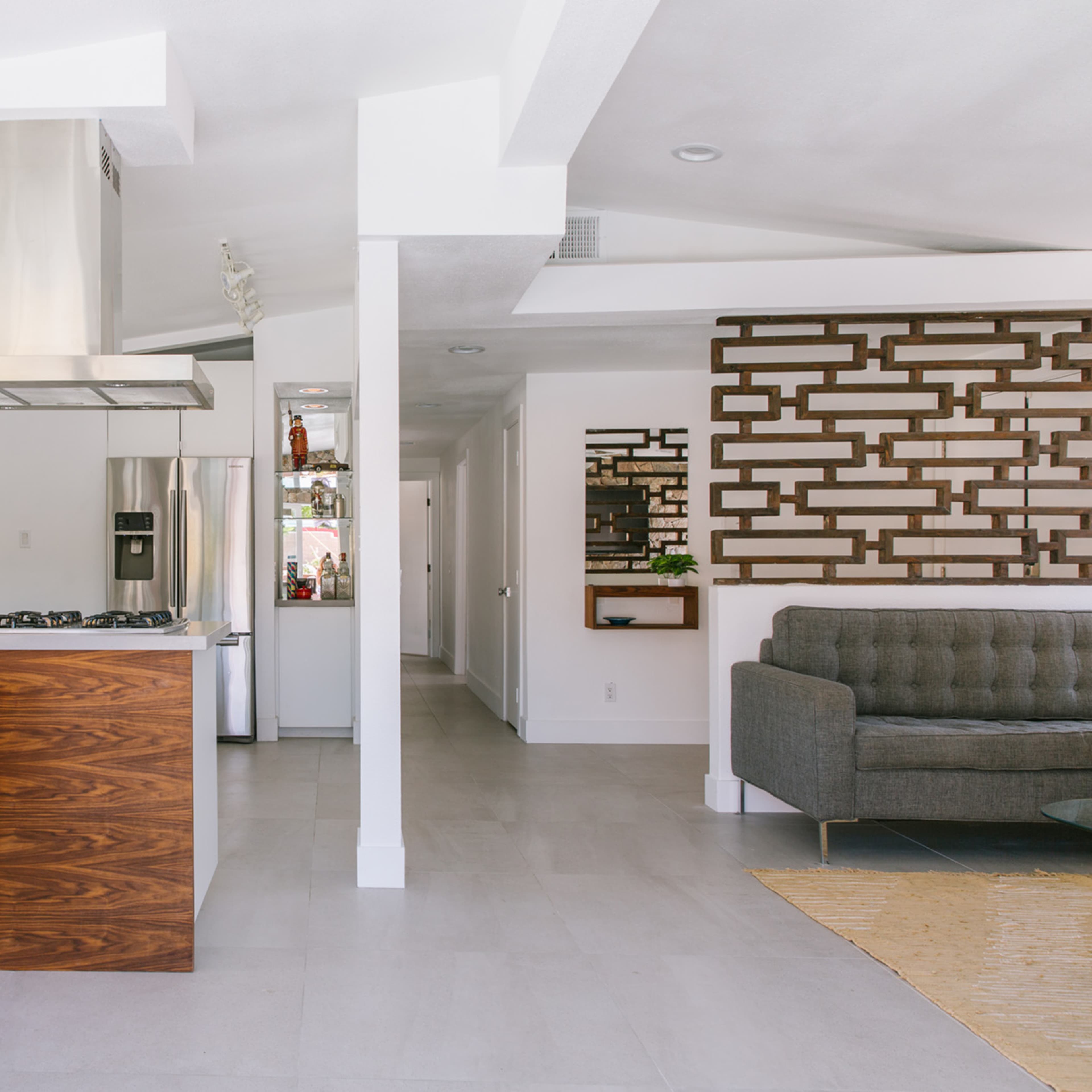 A modern kitchen and living area showcase a stainless steel range hood, wooden cabinetry, and red dining chairs adjacent to a textured wall panel.