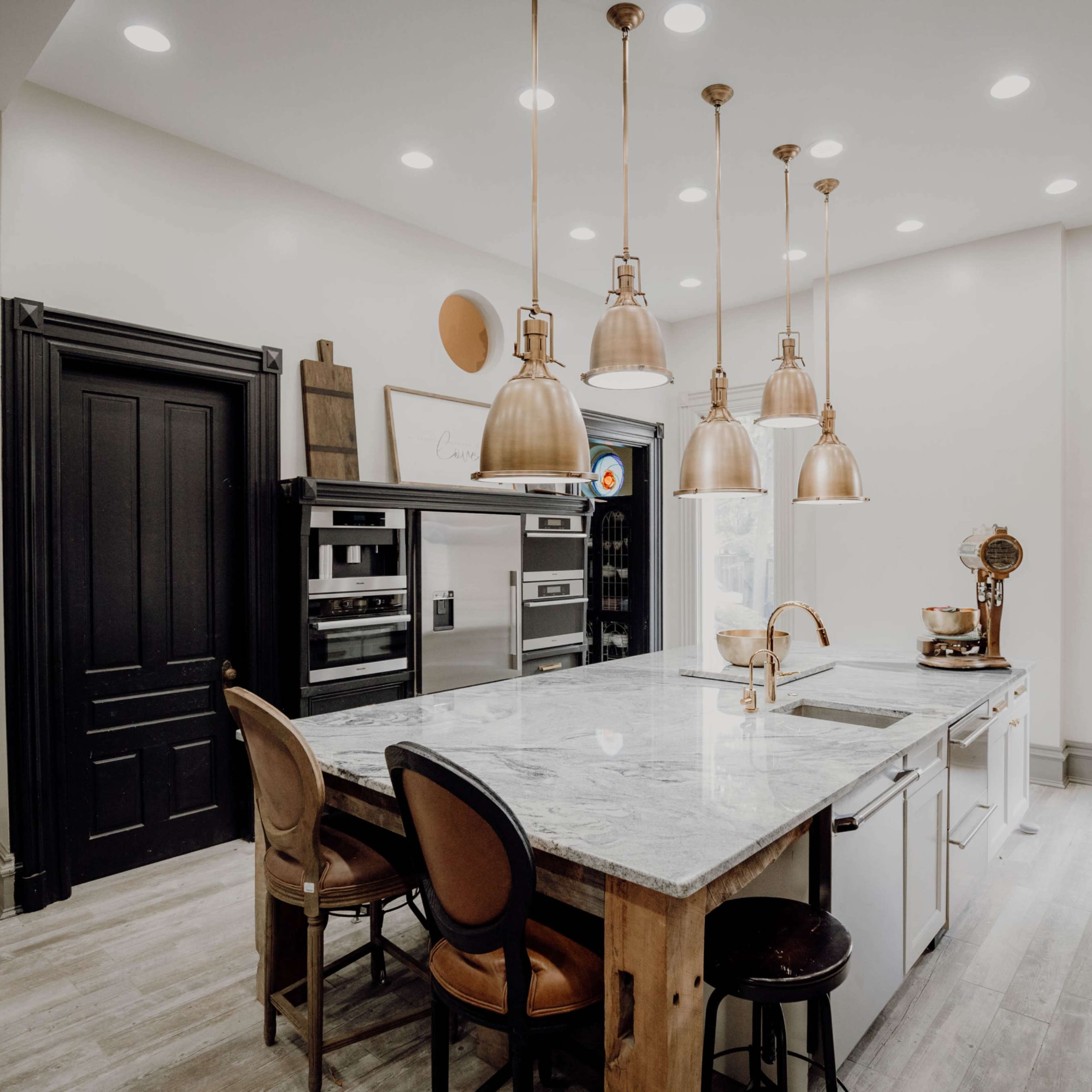 A modern kitchen features a large island with seating, pendant lights above, and stainless steel appliances.
