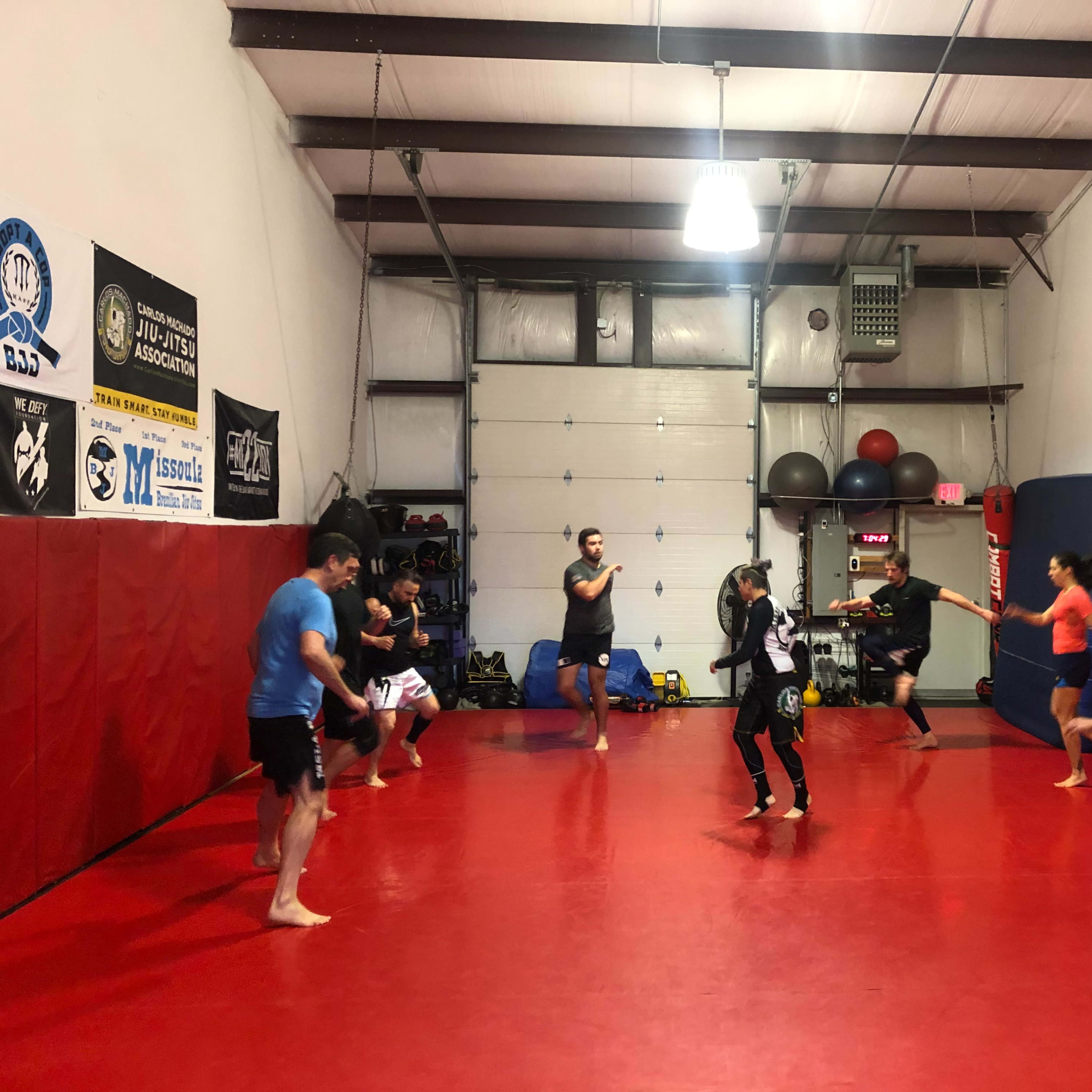 A group of people practice martial arts in a dojo with red mats and various training equipment.