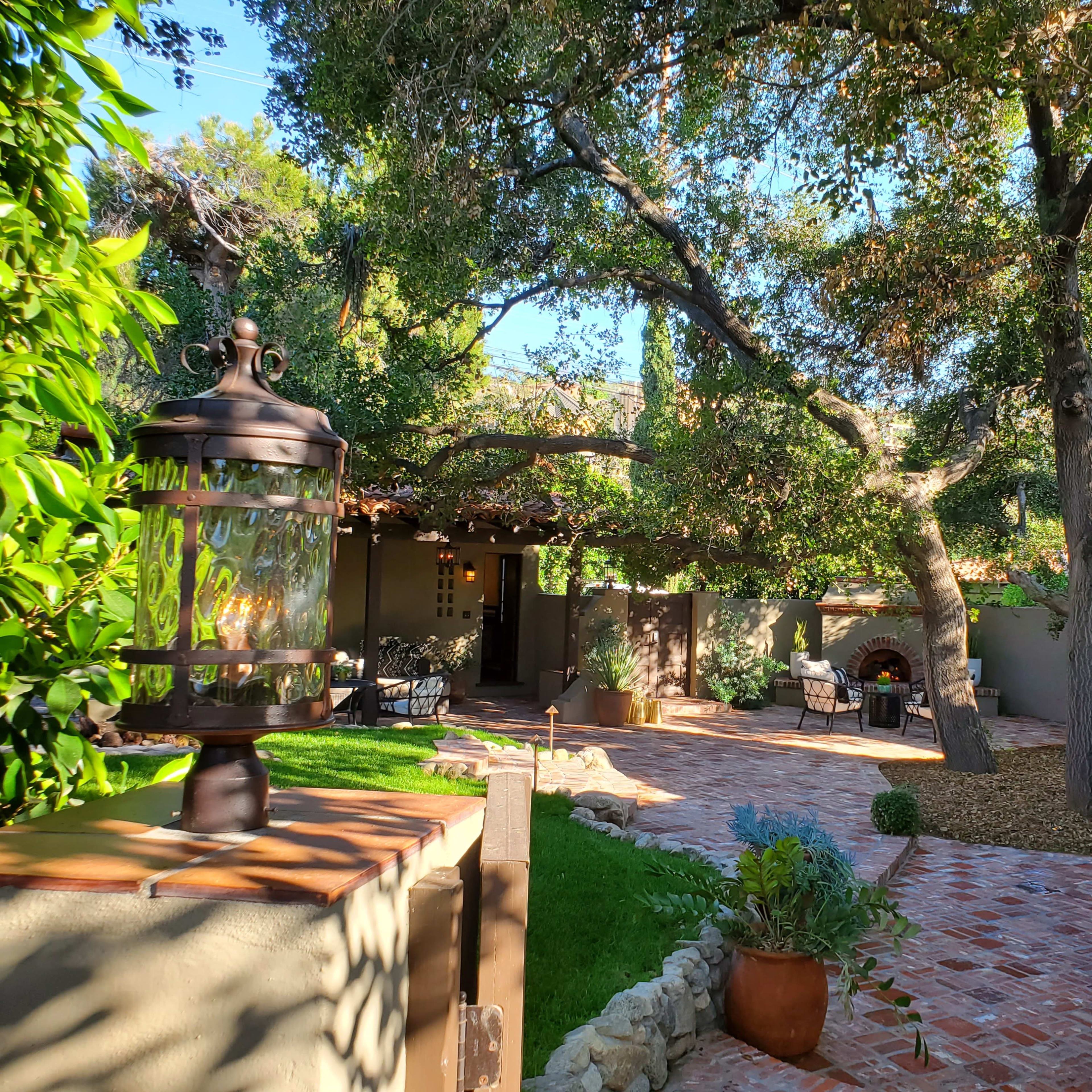 A landscaped garden area with stone pathways, seating arrangements, and large trees providing shade.