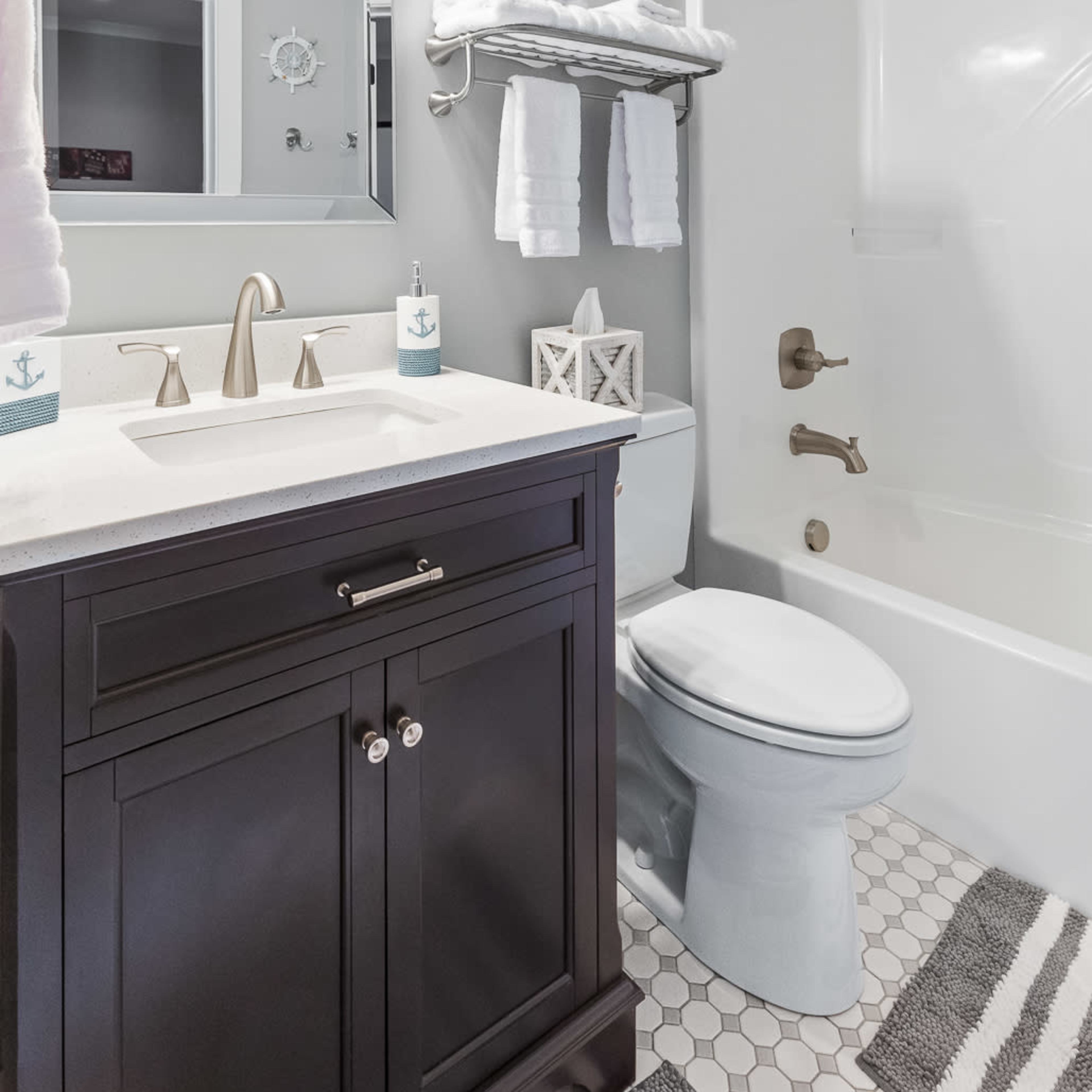 A modern bathroom featuring a dark vanity with a countertop sink, a mirror above it, towels on a rack, and a bathtub with a shower.