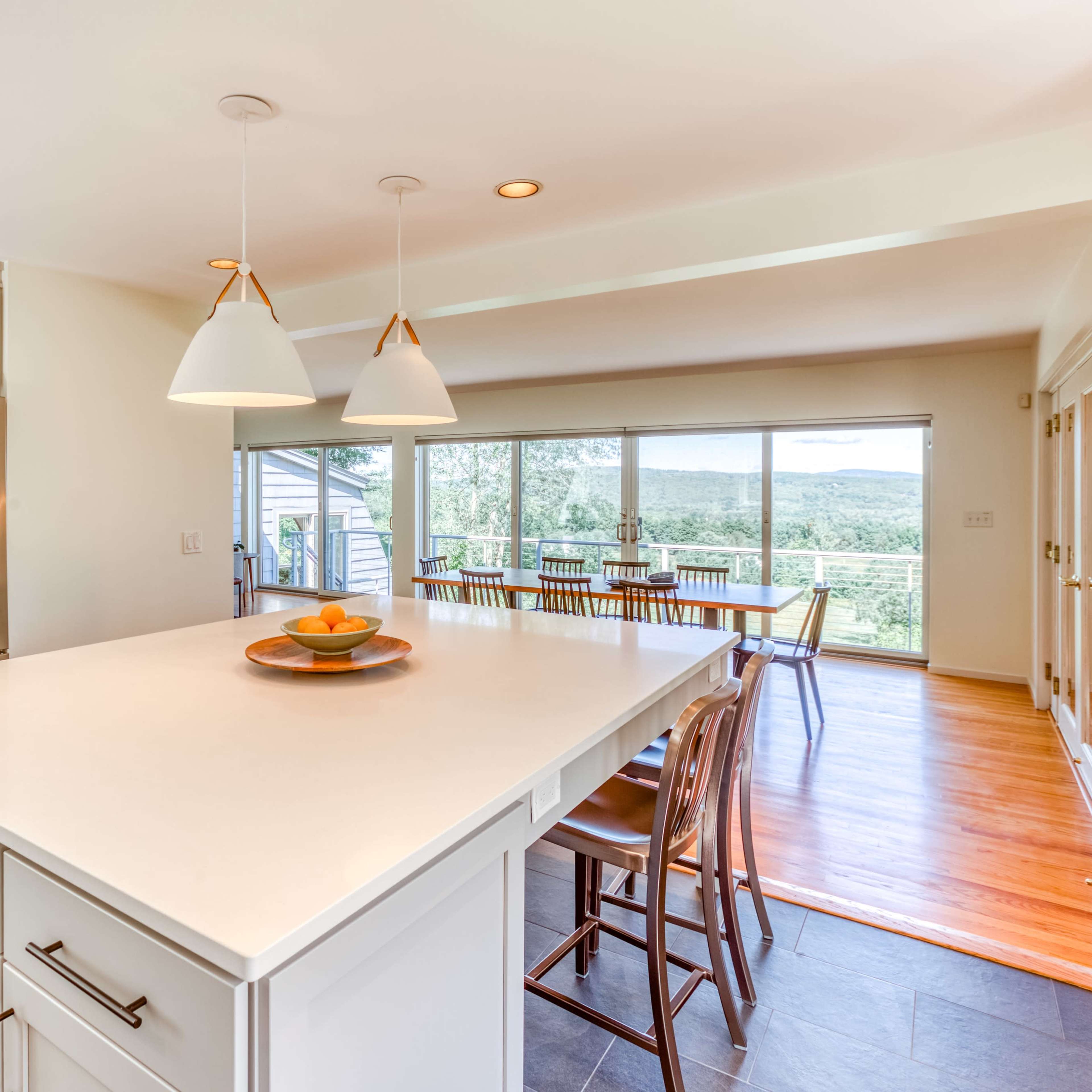 A modern kitchen features a large island with seating, stainless steel appliances, and floor-to-ceiling windows offering a view of the landscape.