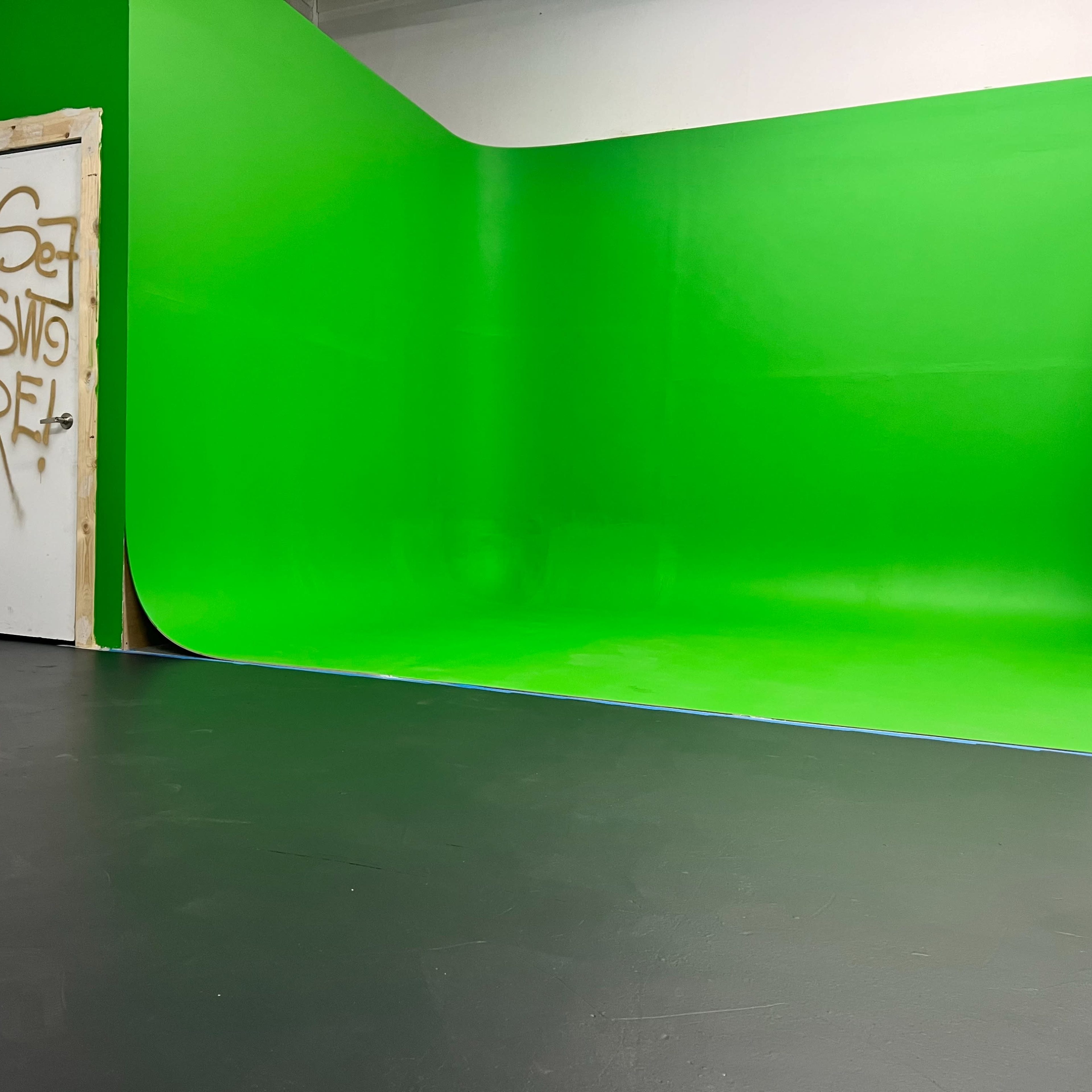 A studio space with a green backdrop and a door featuring graffiti.