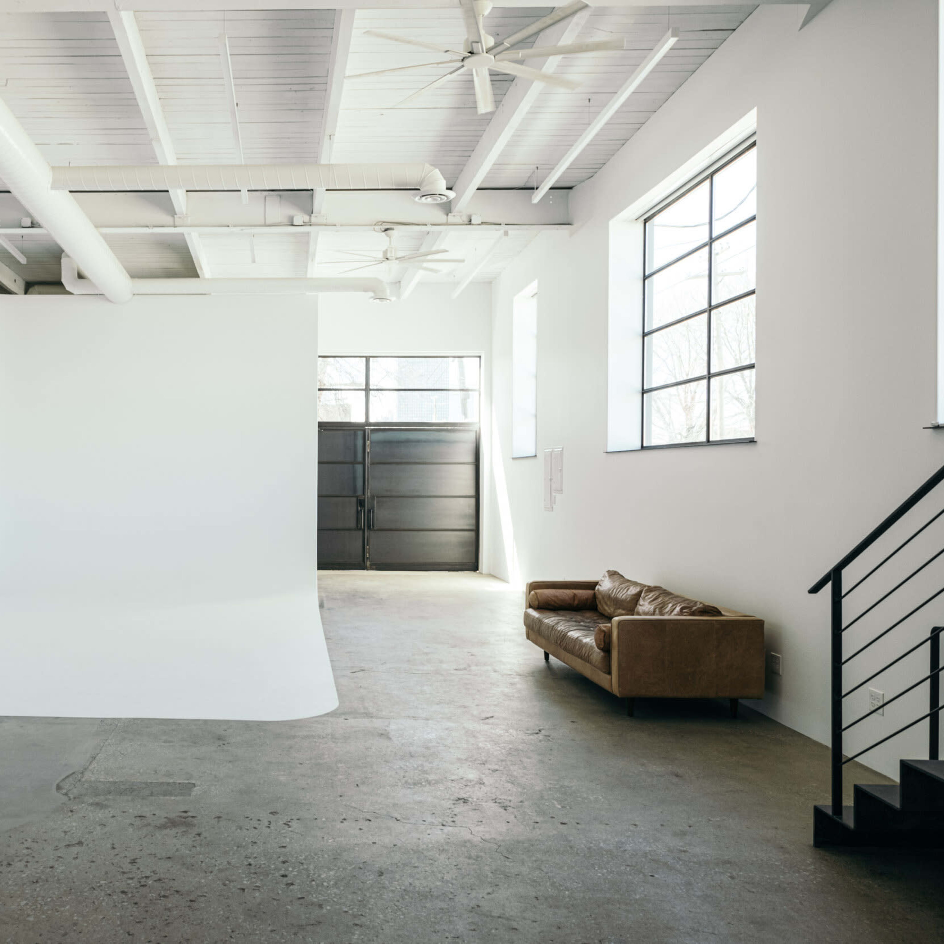 A large, empty studio space features a seamless white backdrop and a brown leather couch against a concrete floor.