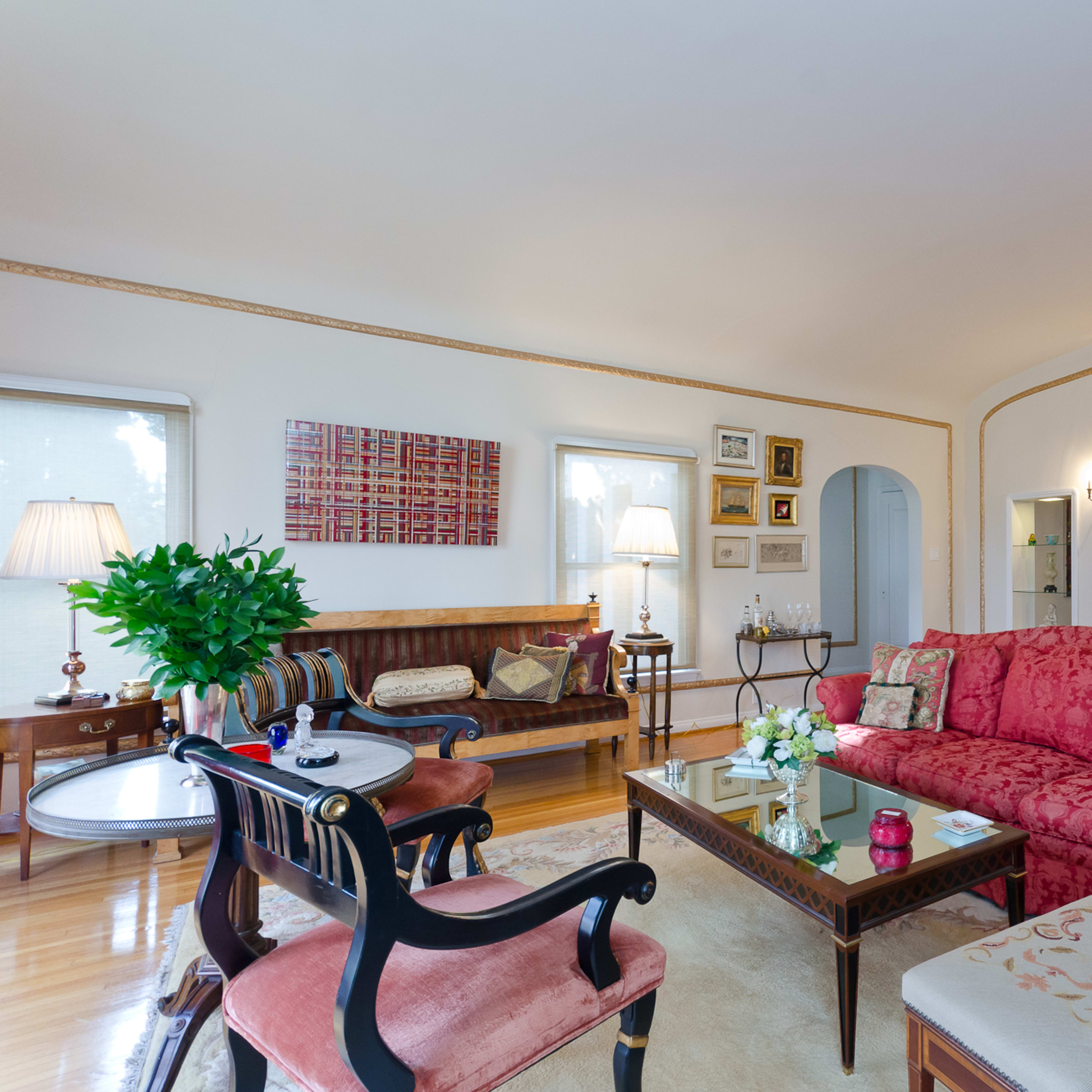 A spacious living room featuring a pink floral sofa, a wooden piano, and various decorative elements on the walls.