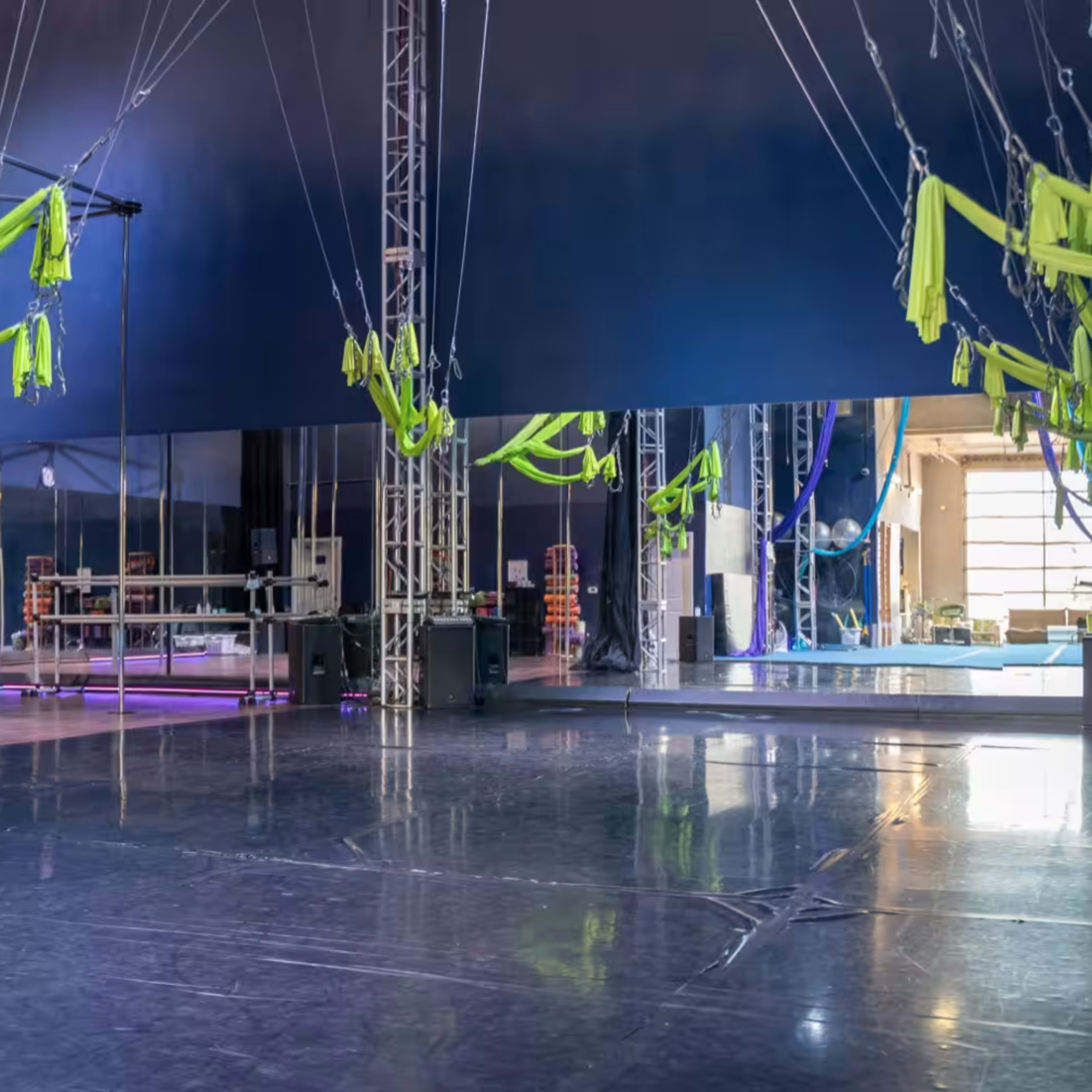 A spacious studio with a polished floor features hanging green fabric and large mirrors along one wall.