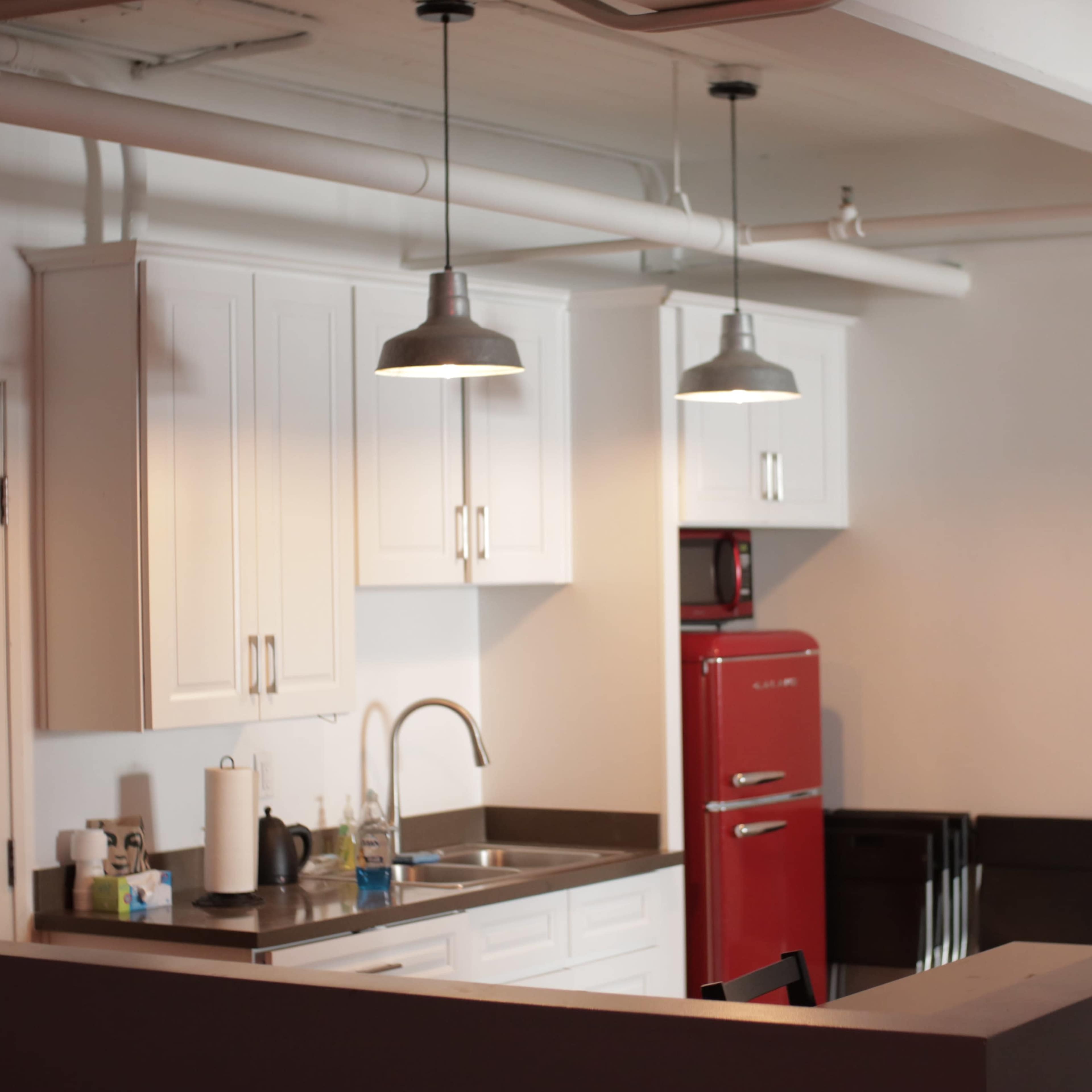 A modern kitchen featuring white cabinets, a red refrigerator, and metallic pendant lights hanging above the countertop.