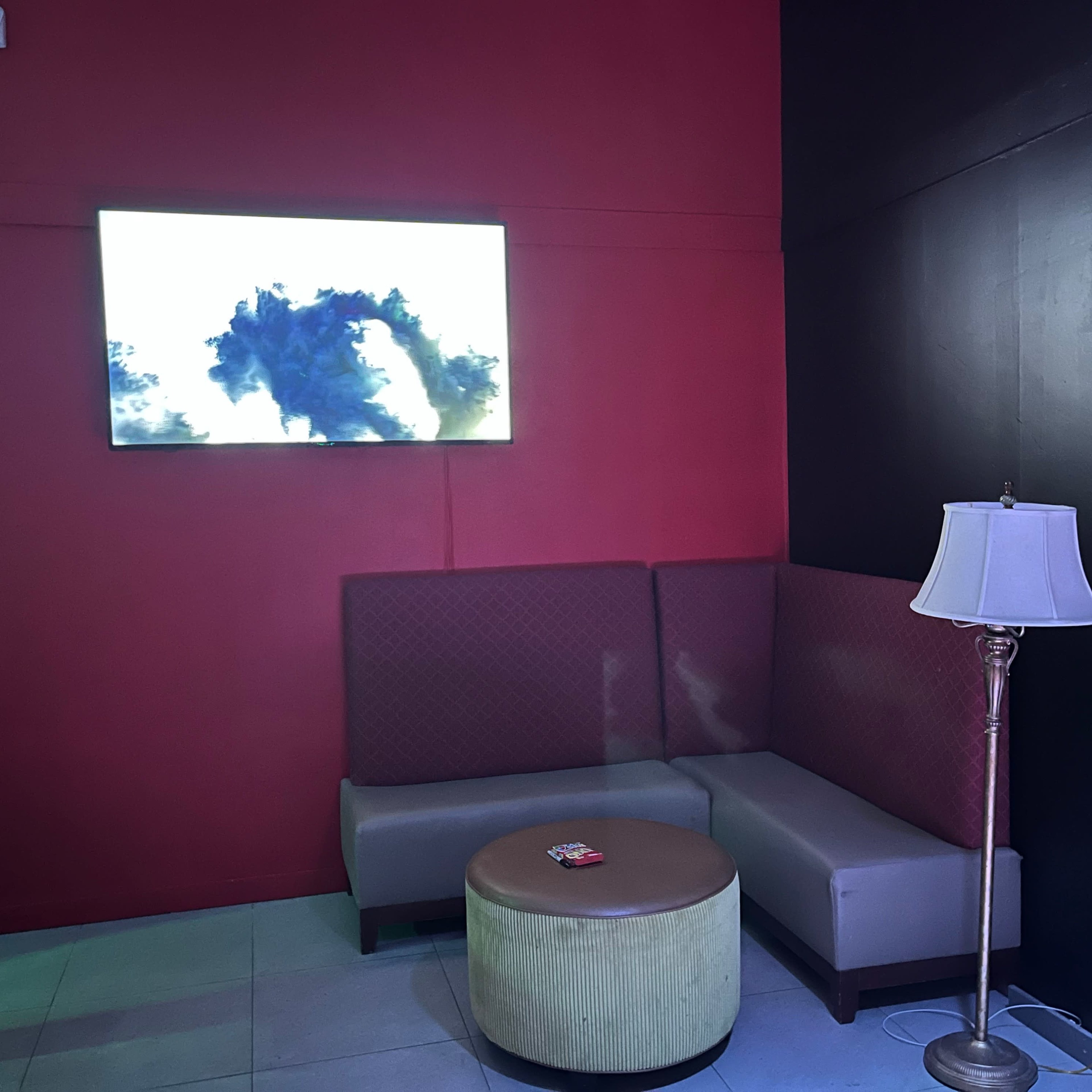 A corner of a room featuring a TV on a red wall, a round coffee table, a lamp, and a cushioned seating area.