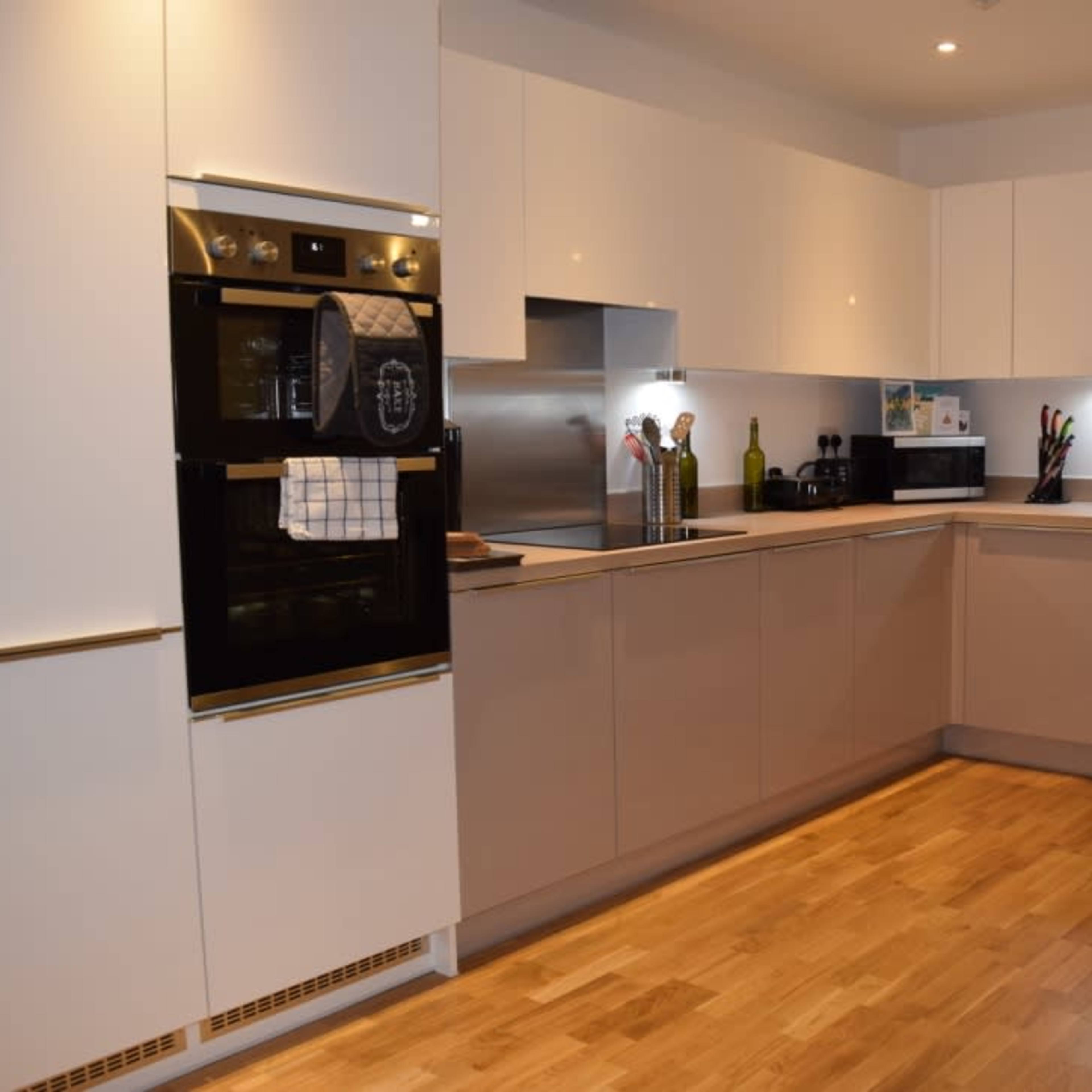A modern kitchen with light-colored cabinetry, stainless steel appliances, and a wooden floor.