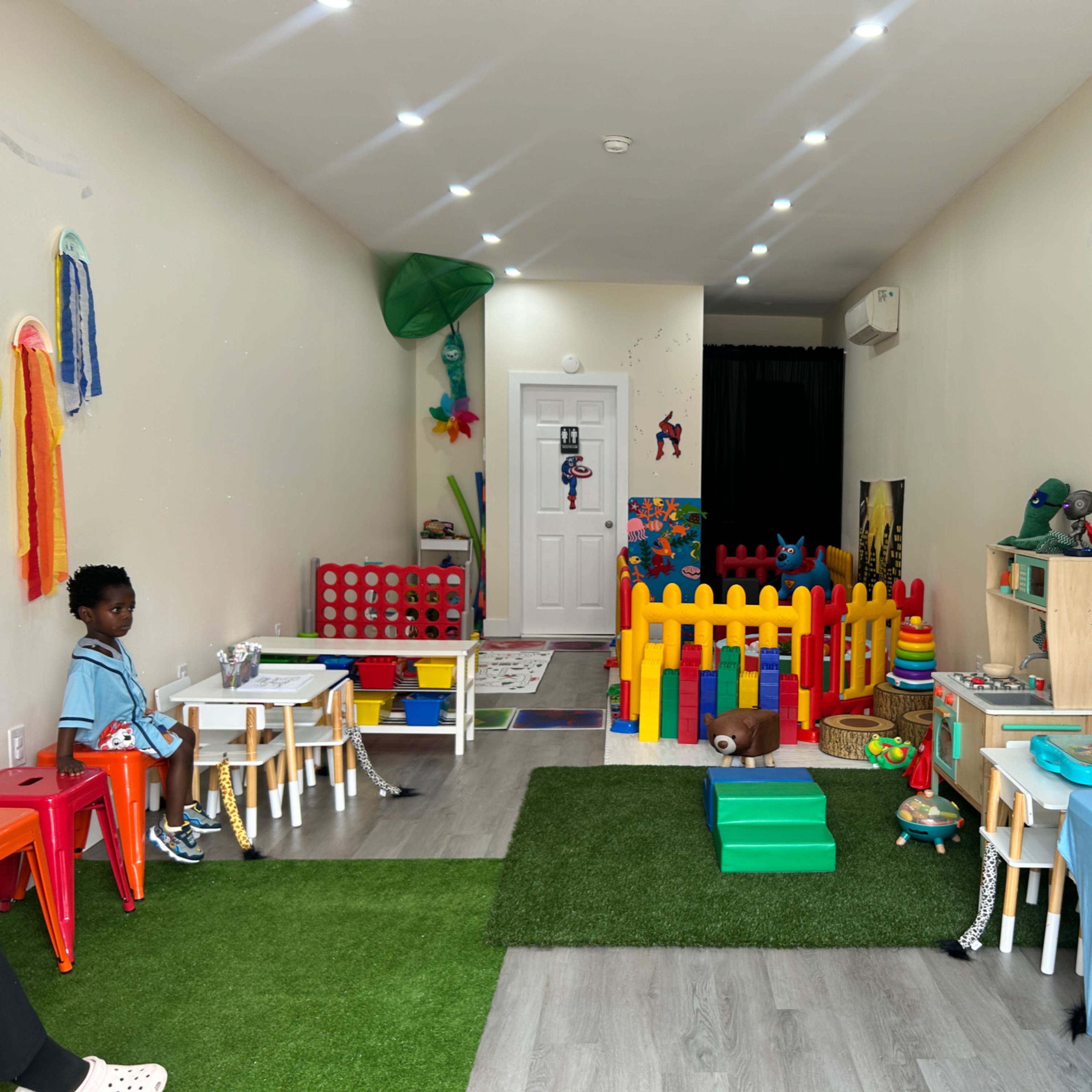 A colorful playroom with children's tables and chairs, a fenced play area, and various toys spread across the floor.