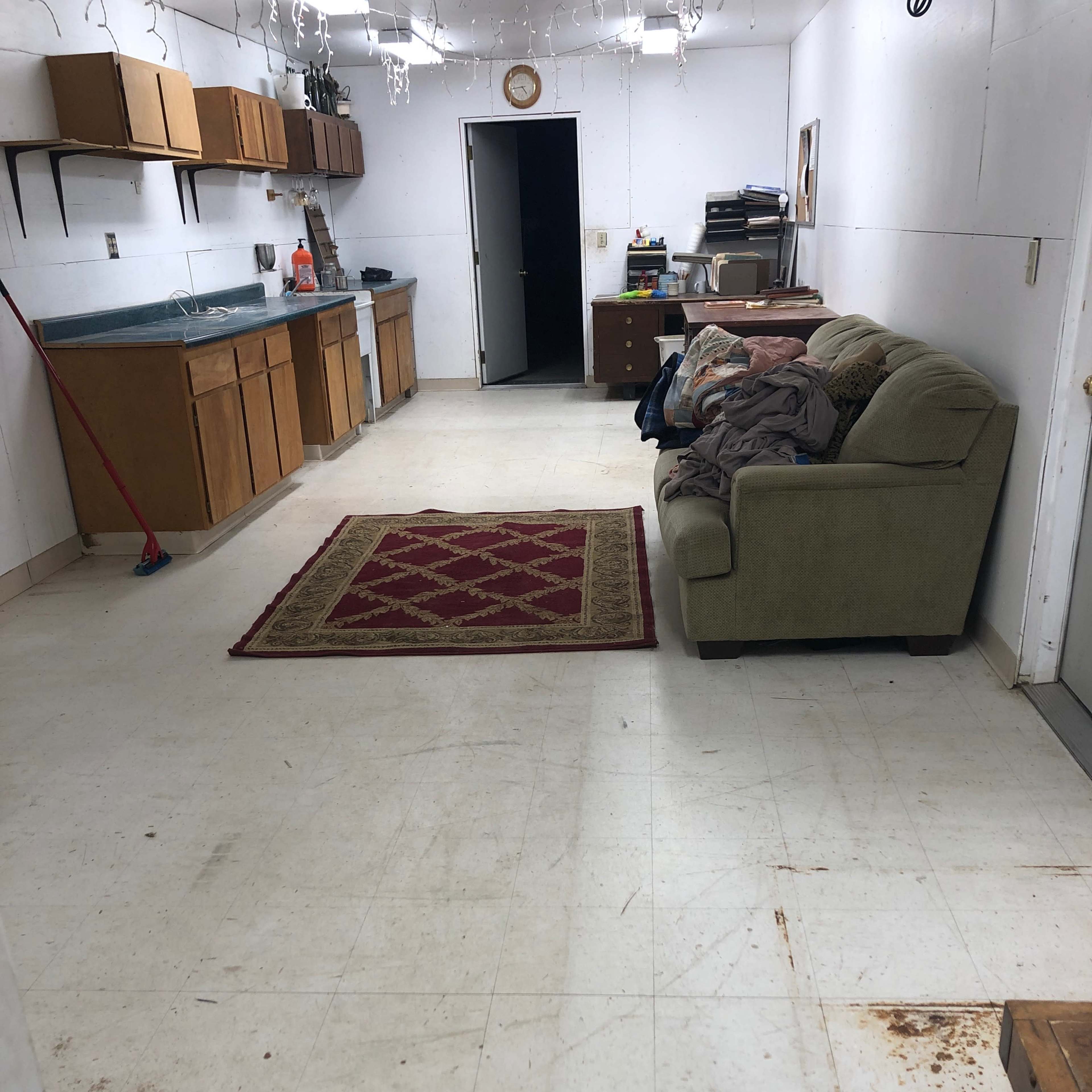 A spacious room with a kitchen area, a couch, and a red patterned rug on a tiled floor.