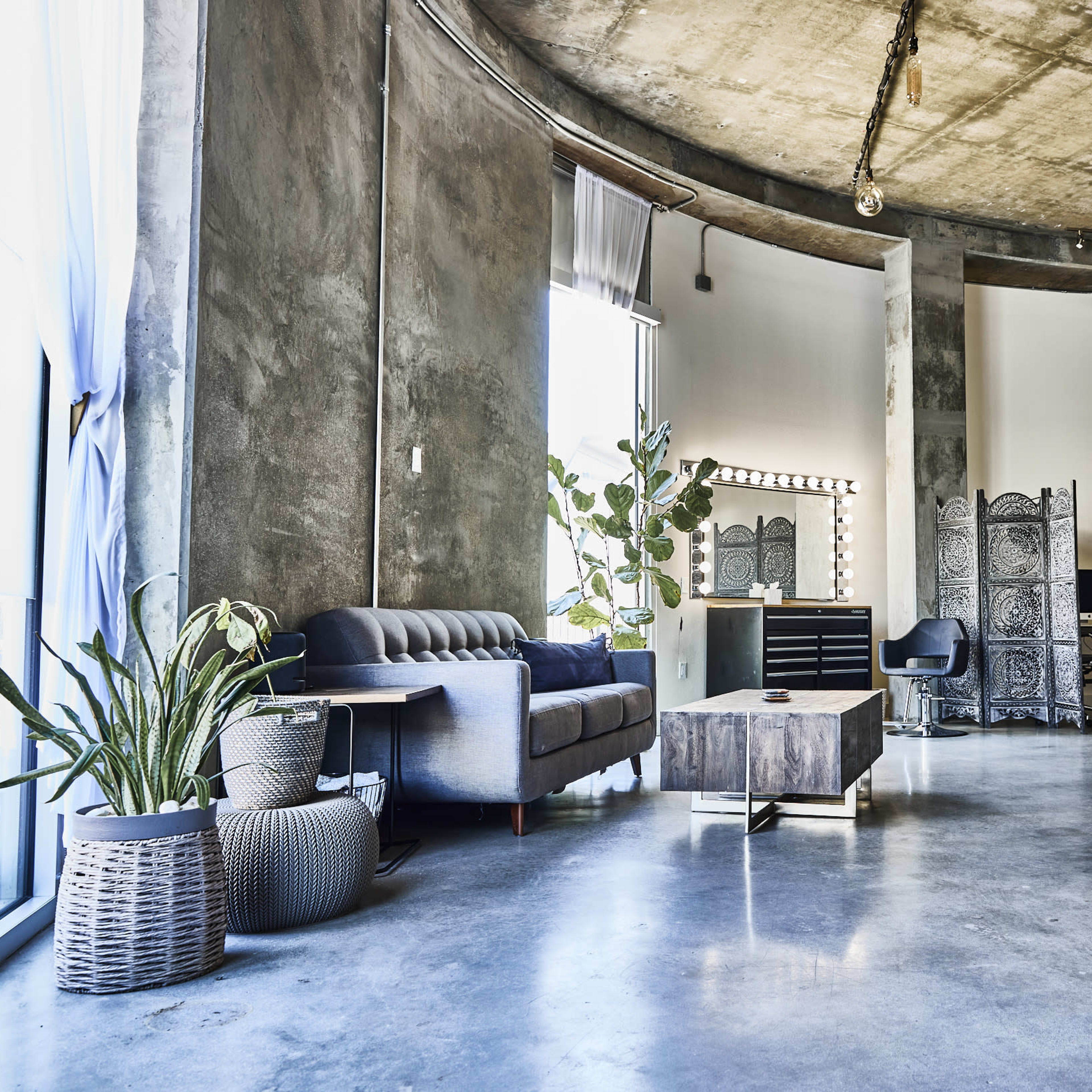 A modern industrial living space with concrete walls, a round ceiling, and a combination of seating furniture, a coffee table, and decorative plants.