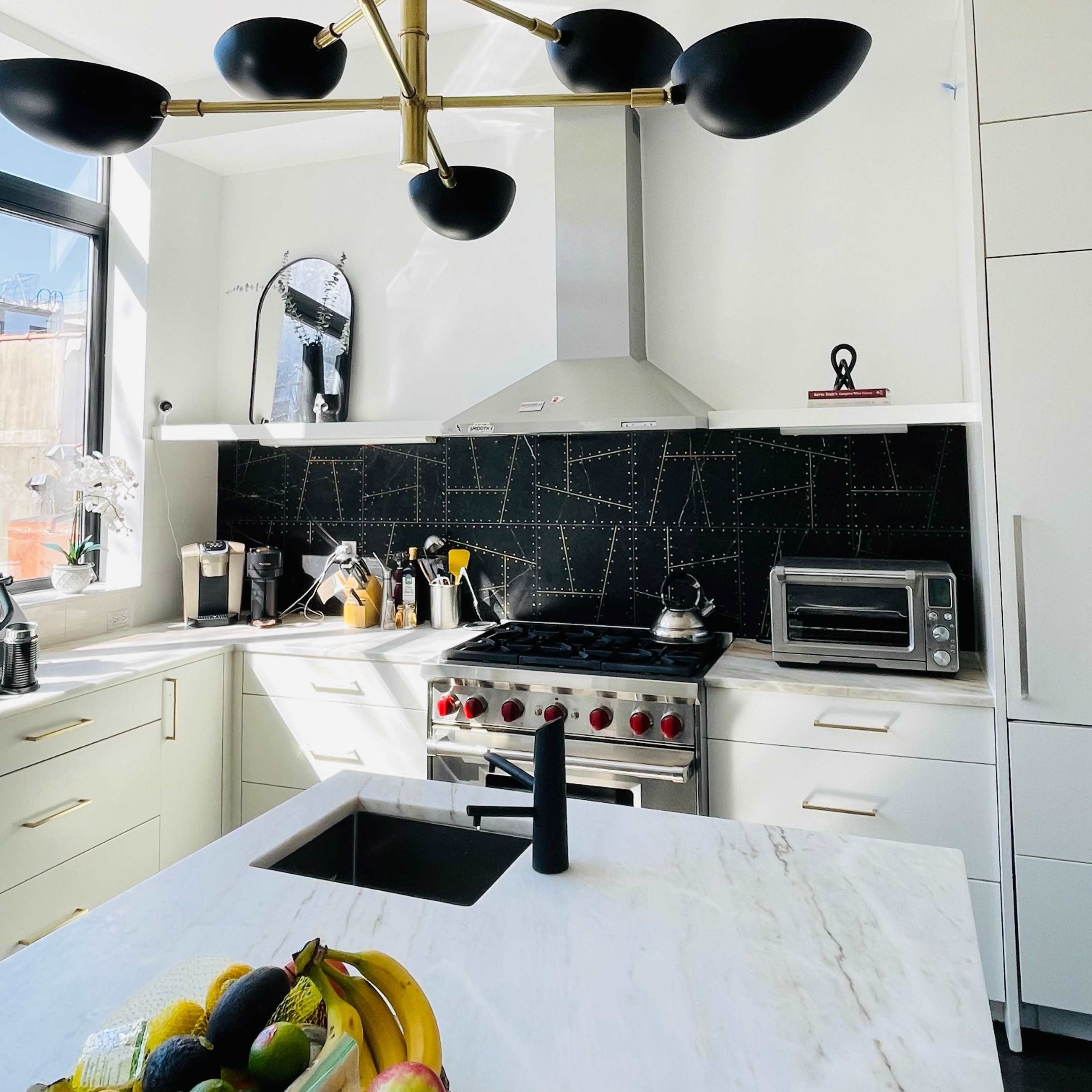 The kitchen features a central black chandelier, stainless steel appliances, and a marble countertop with a fruit bowl.