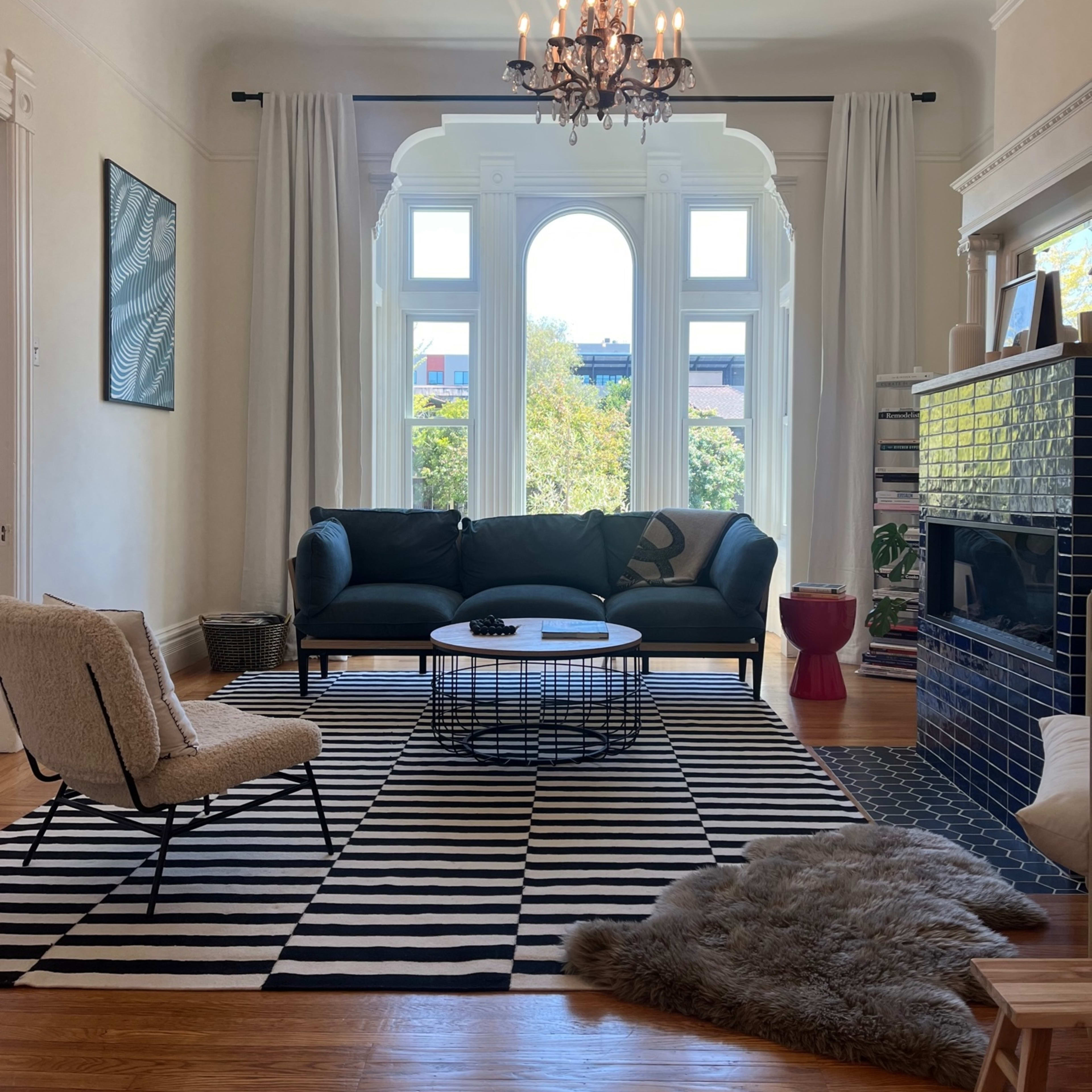 A stylish living room featuring a dark sofa, a round coffee table, and a patterned rug, with large windows letting in natural light.