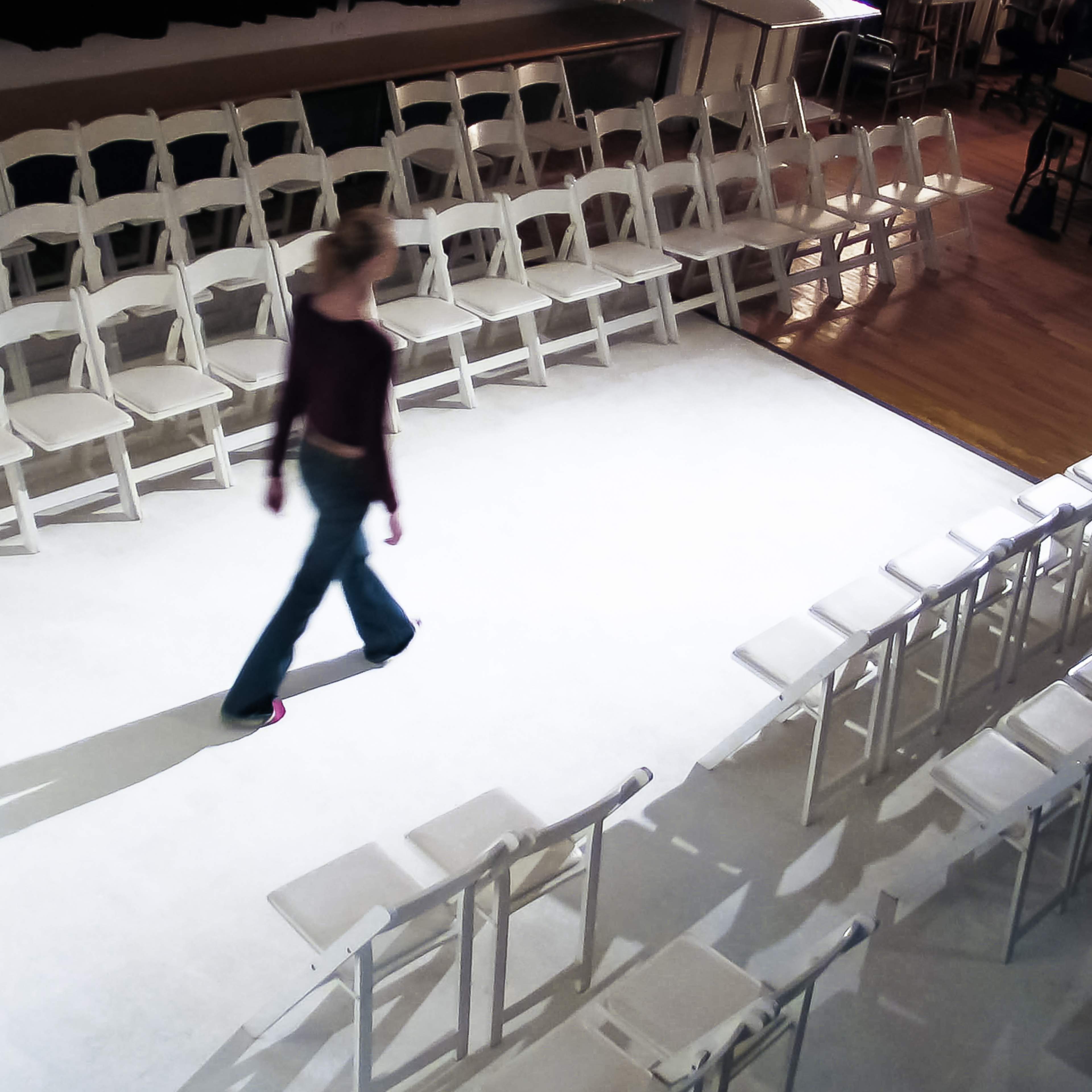 A person walks along a runway surrounded by multiple rows of white chairs.