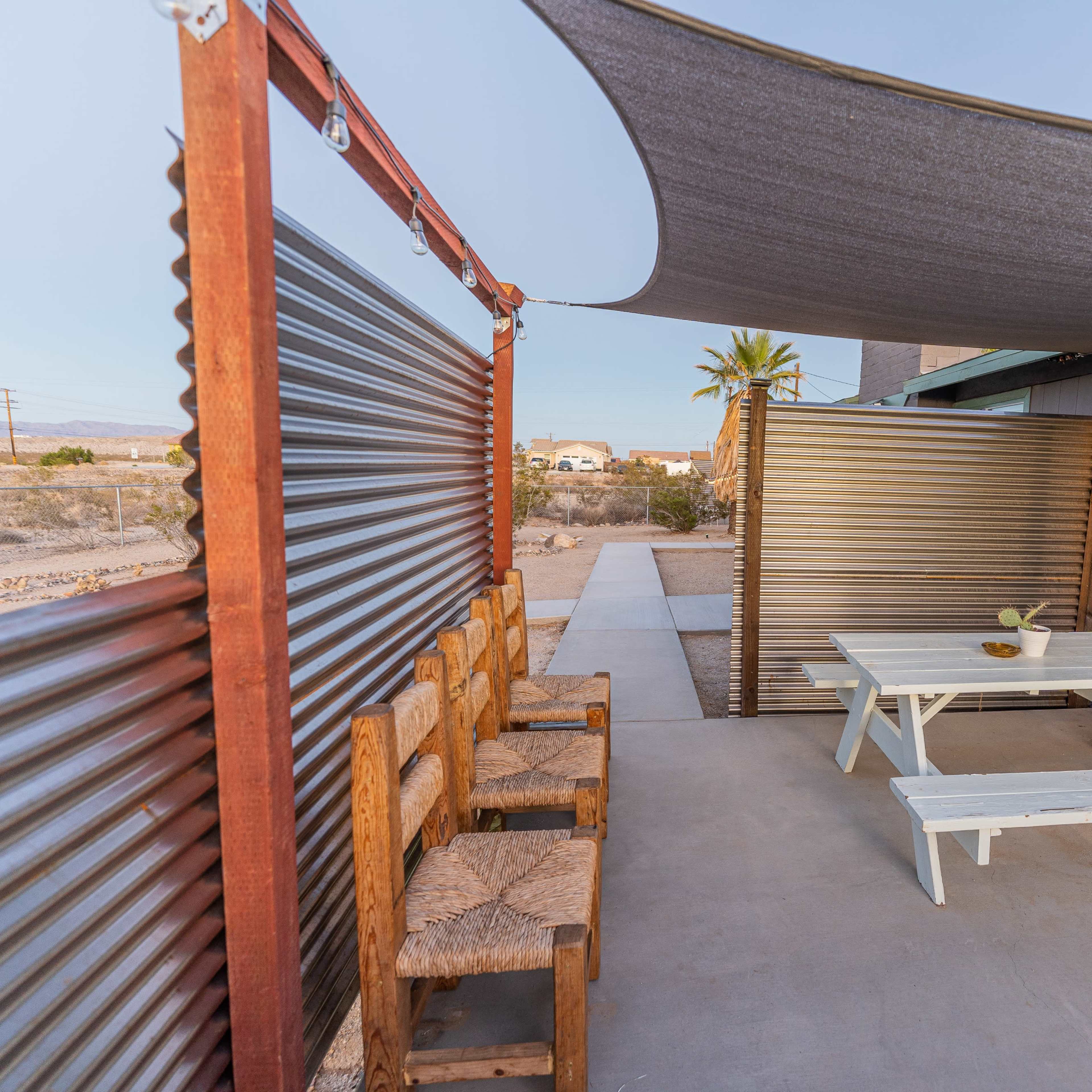 A patio area features a picnic table surrounded by rustic seating and shaded by a gray canopy.