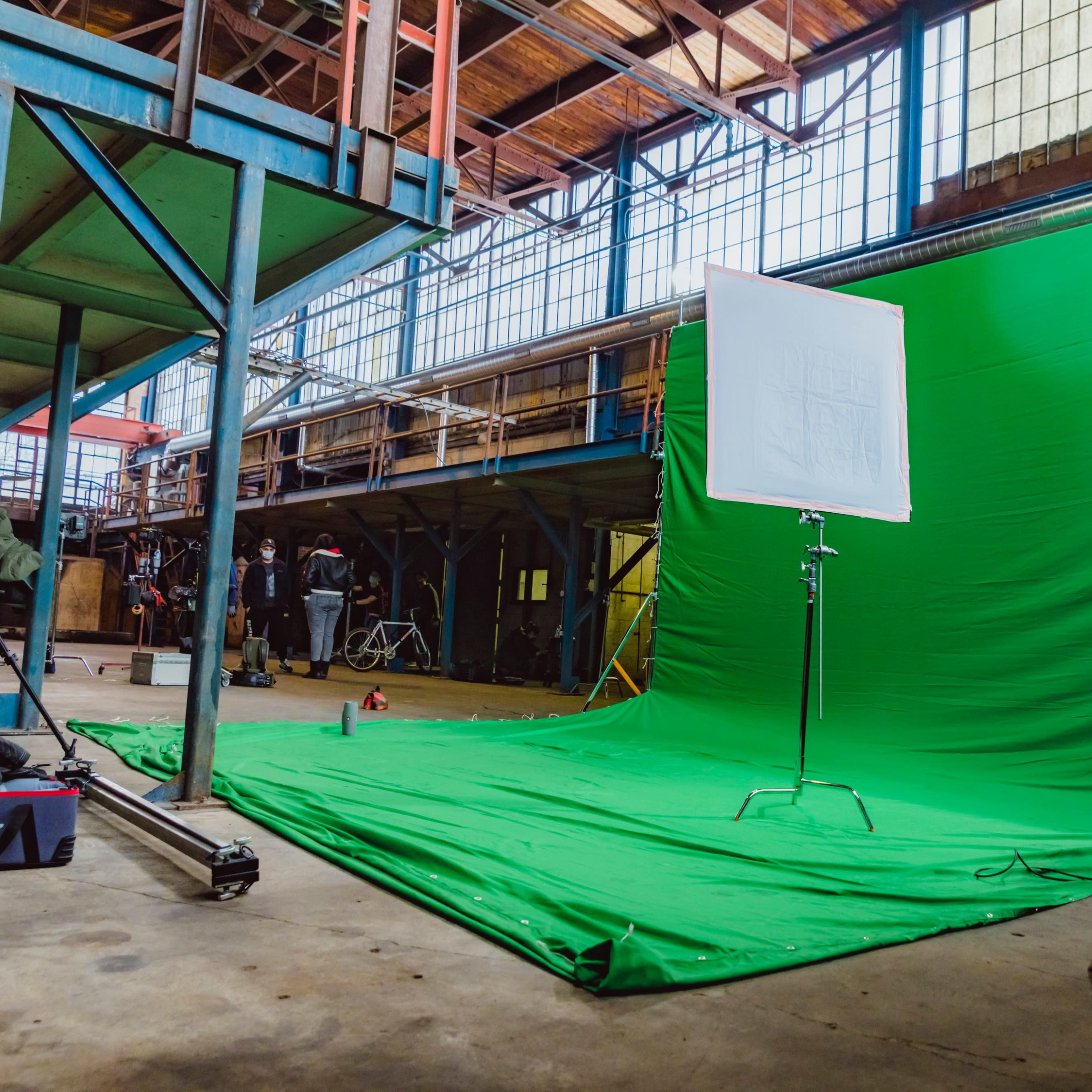 A photography studio space with a green screen backdrop set up on a concrete floor, surrounded by various equipment and personnel.