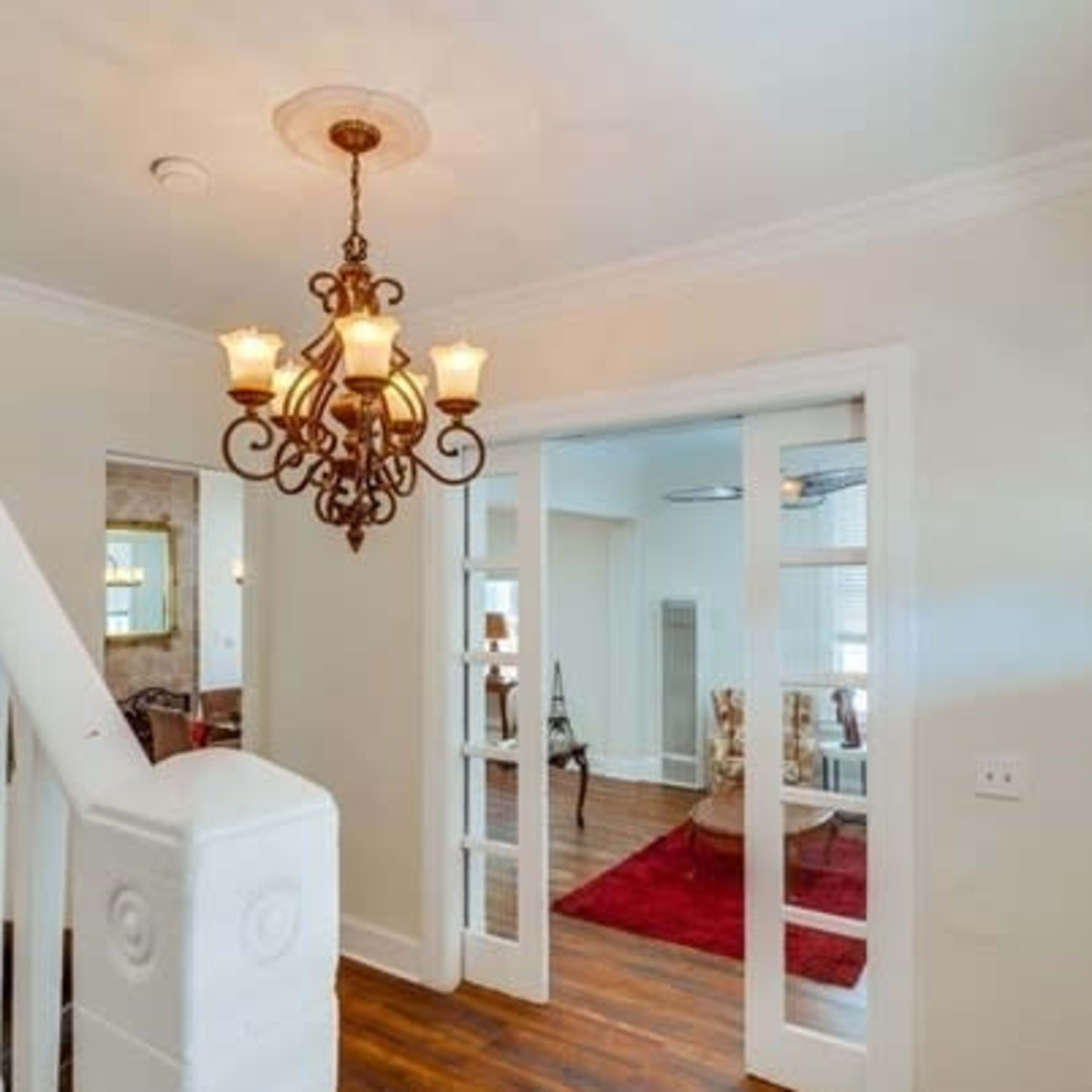 A staircase leads to a well-lit hallway featuring a chandelier and glass-paneled doors opening to a living area.