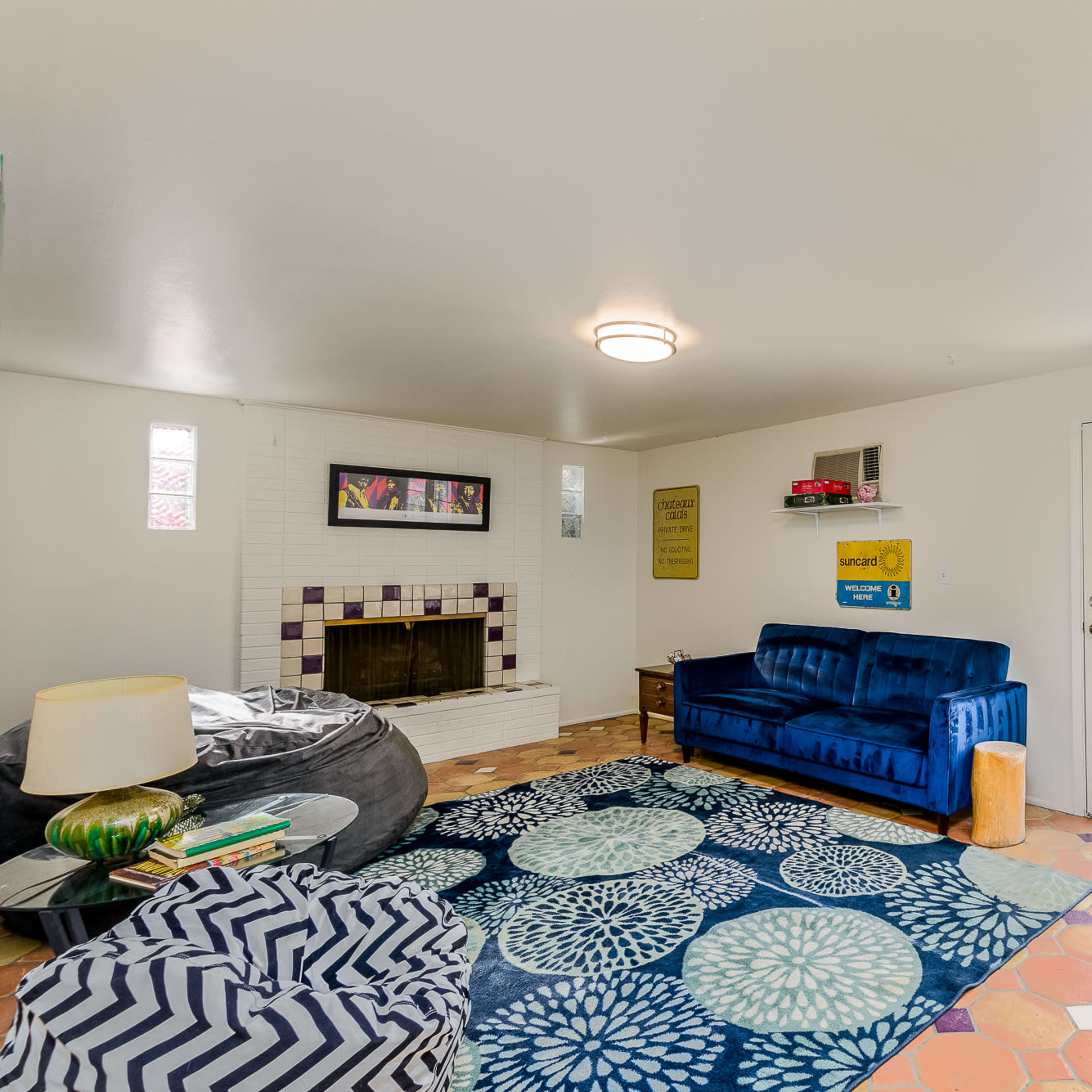The living room features a blue sofa, a large circular chair, a coffee table, and a fireplace surrounded by colorful tiles.