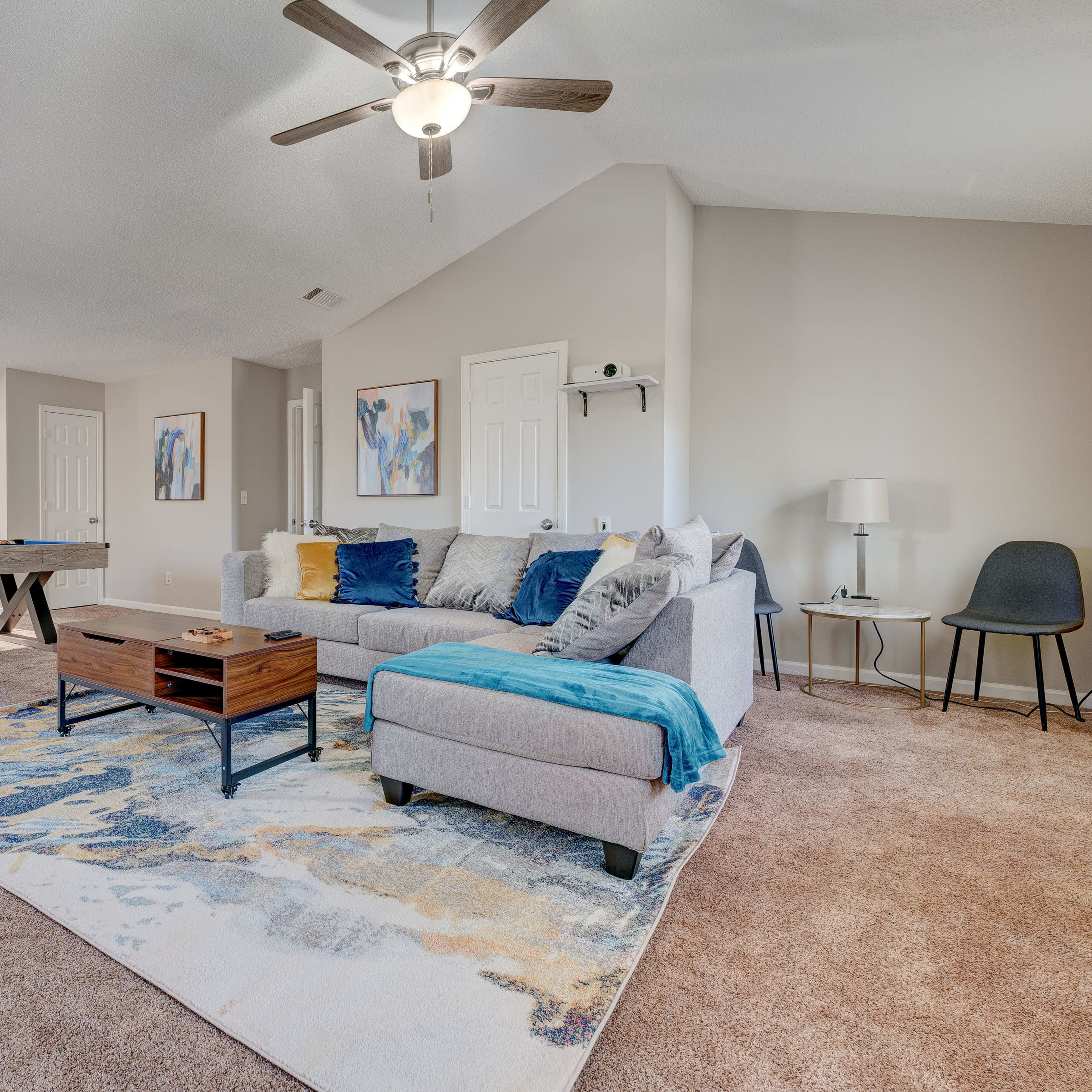 A spacious living area featuring a gray sectional sofa, a coffee table, a patterned rug, and a pool table in the background.
