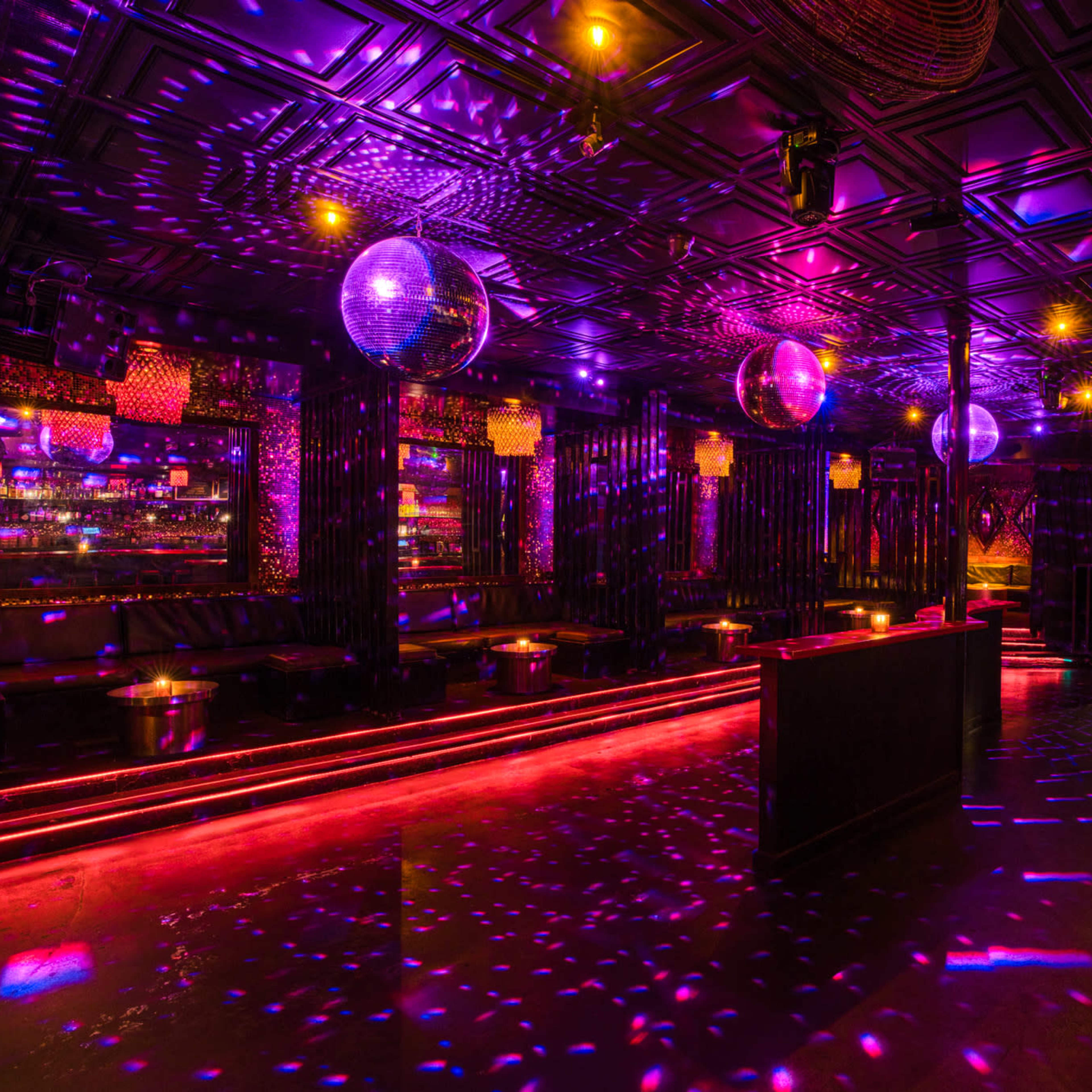 A dimly lit nightclub with colorful lights, disco balls, and a dance floor featuring reflections on the walls and ceiling.