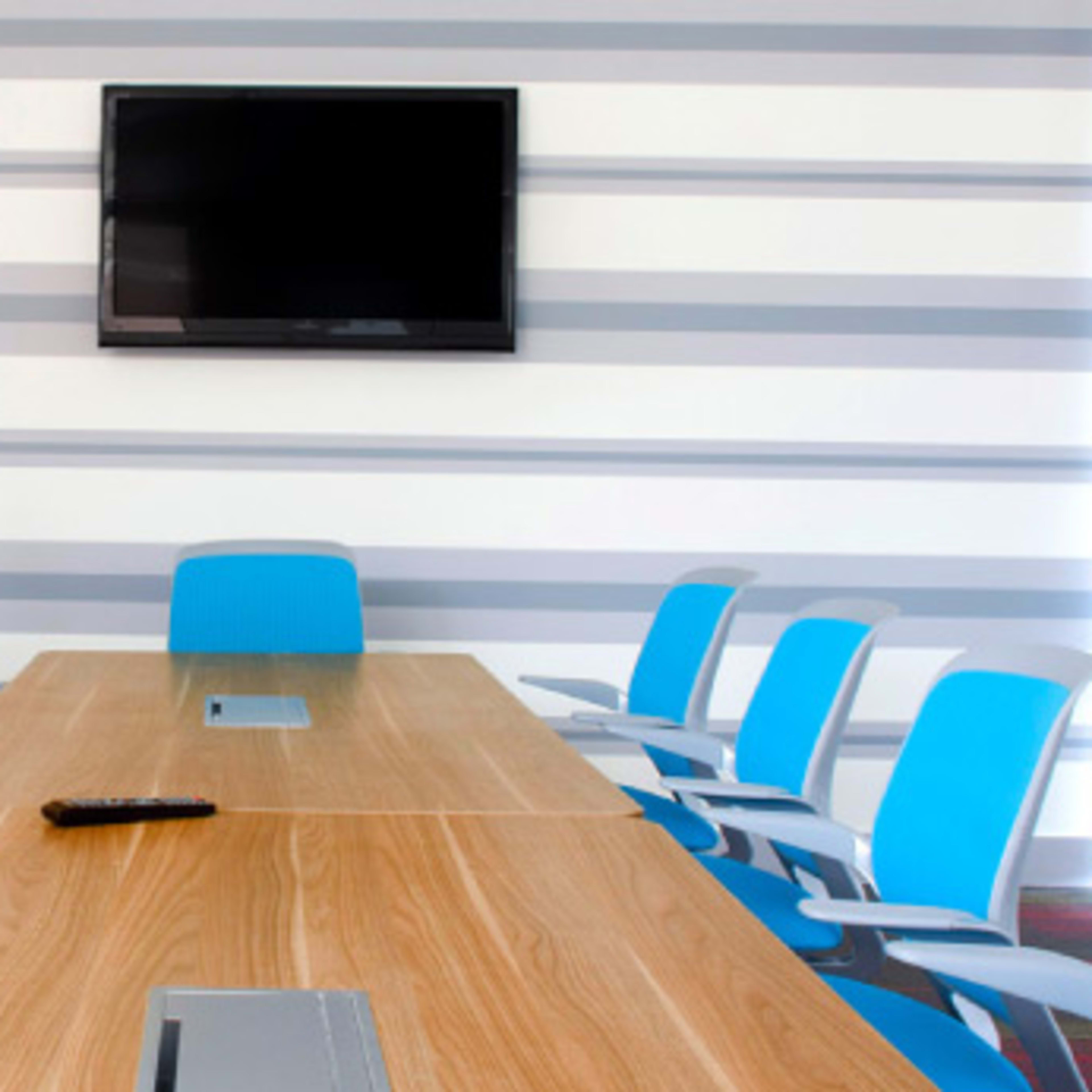 A conference room features a large wooden table surrounded by blue chairs and a wall-mounted television.