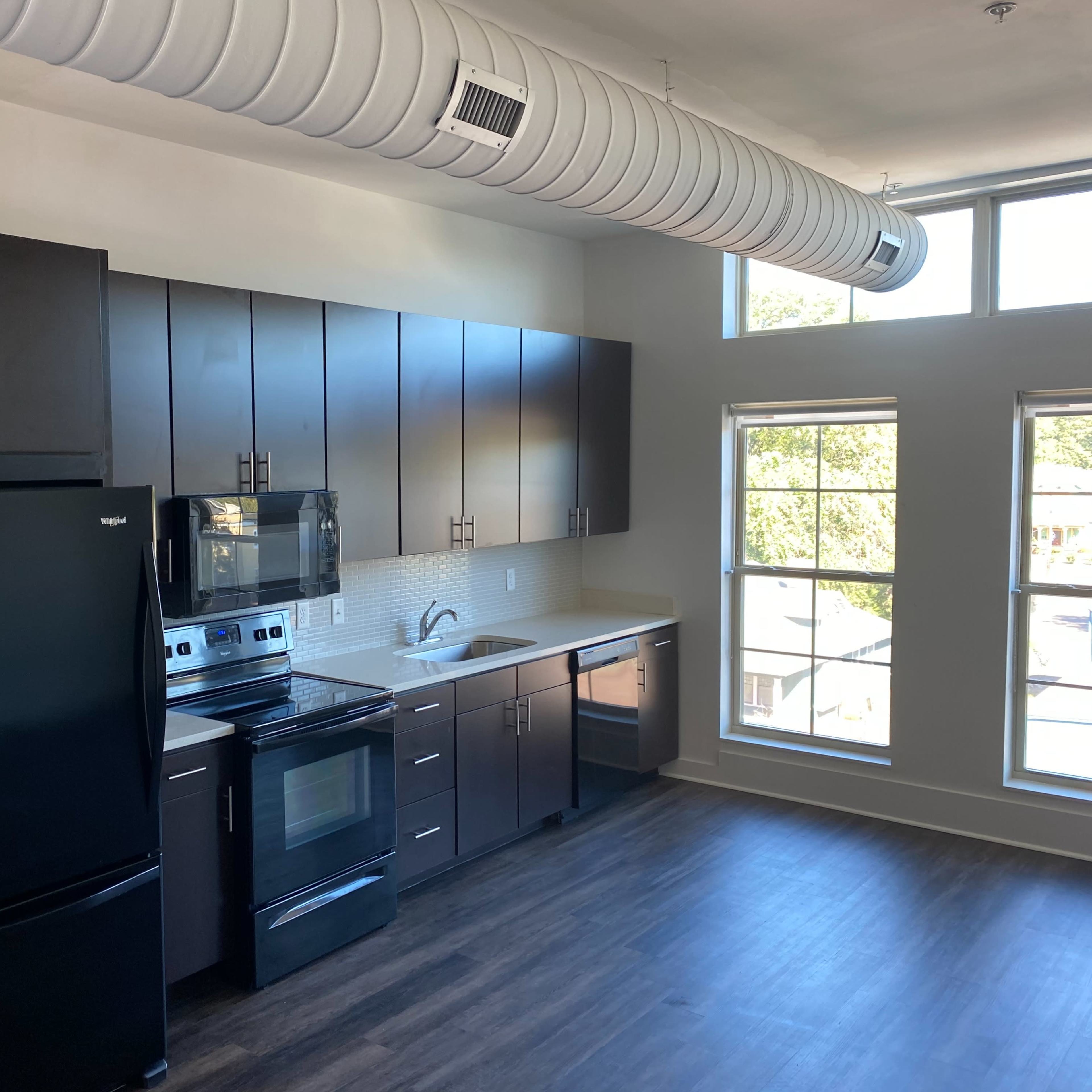 A modern kitchen with dark cabinets, stainless steel appliances, and large windows letting in natural light.