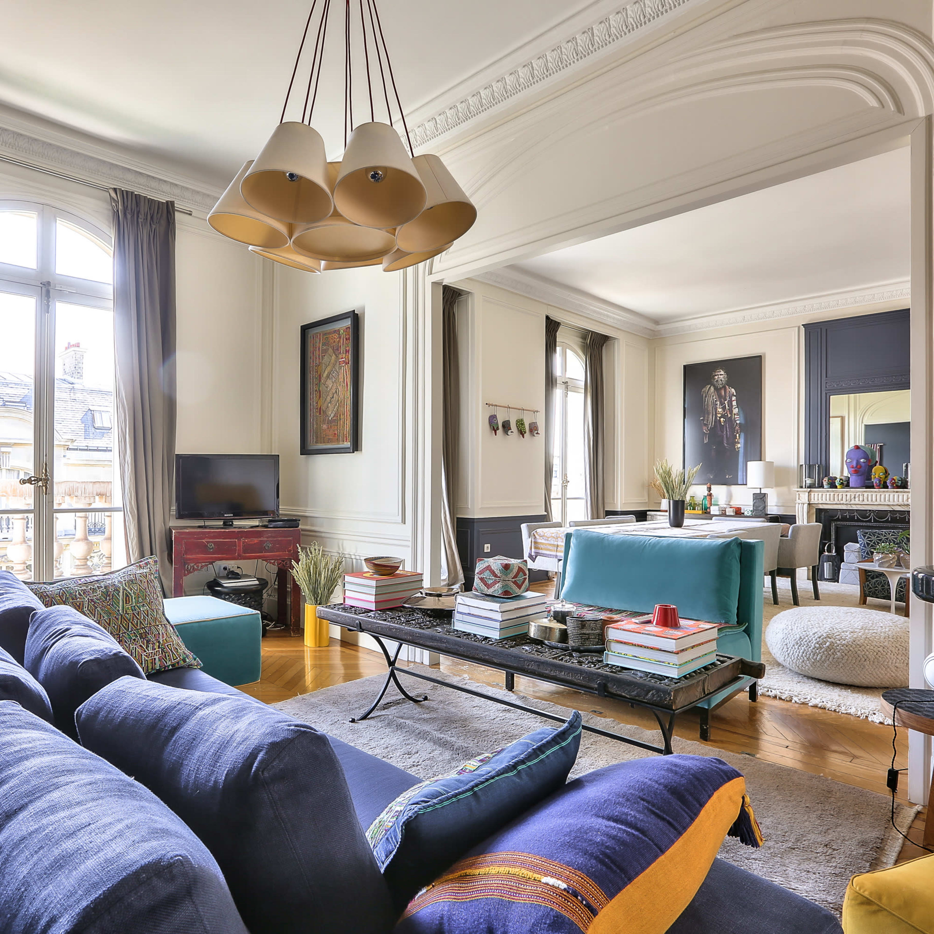 A modern living room features a blue sofa, a coffee table adorned with books and decor, and large windows allowing natural light to fill the space.