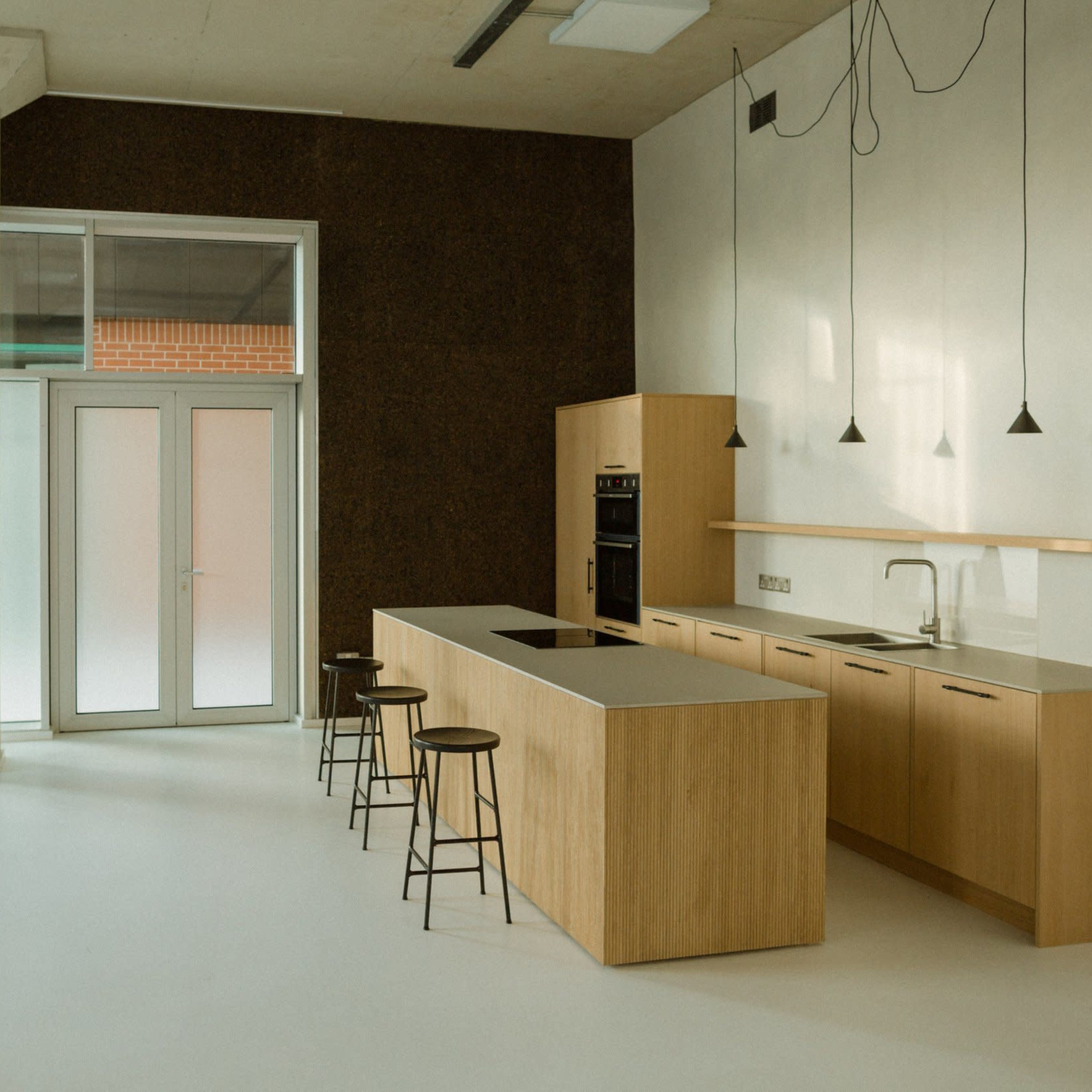 A modern kitchen with a wooden island, bar stools, and minimalistic cabinetry in a spacious, well-lit area.