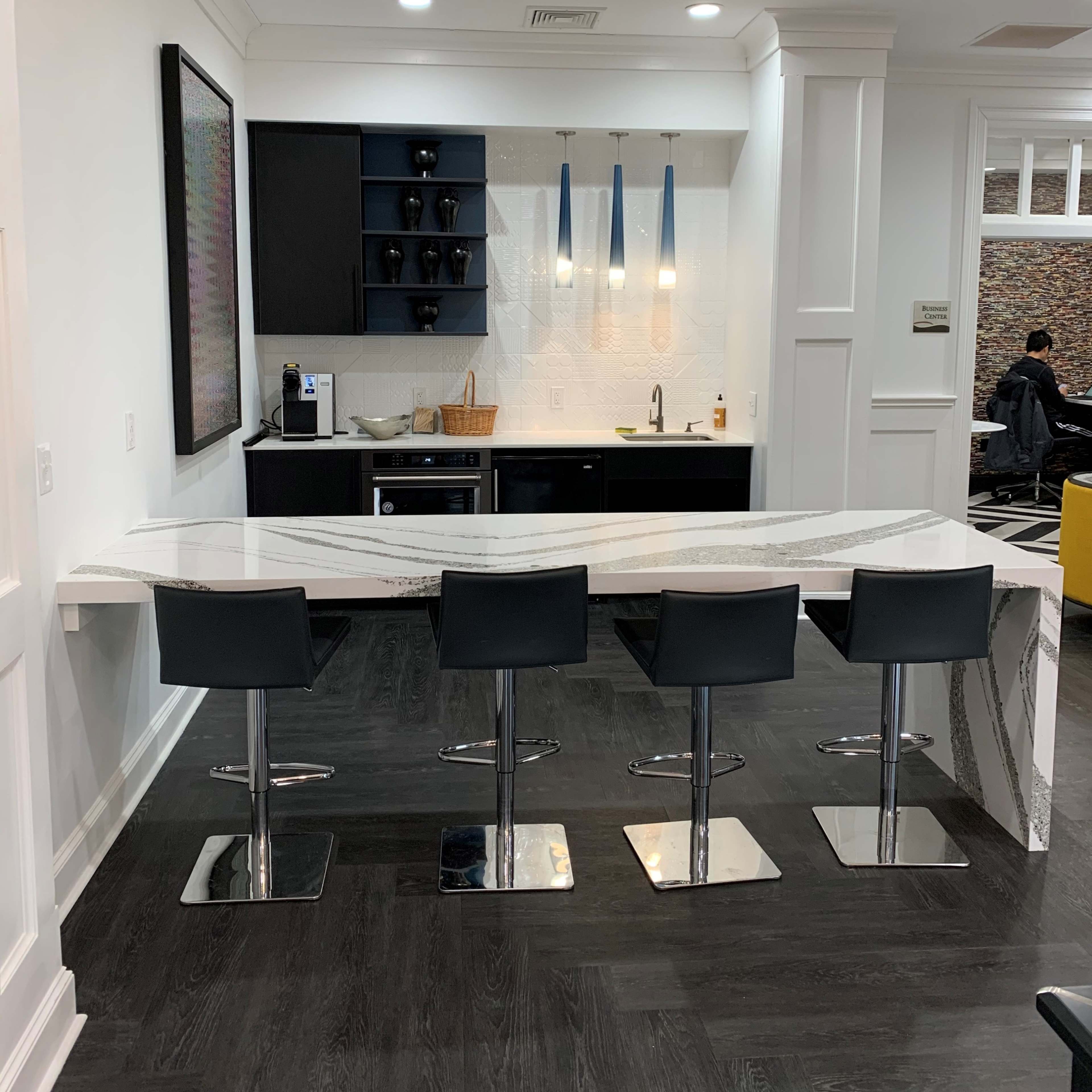A modern kitchen area featuring a curved countertop with four black bar stools and a streamlined design.