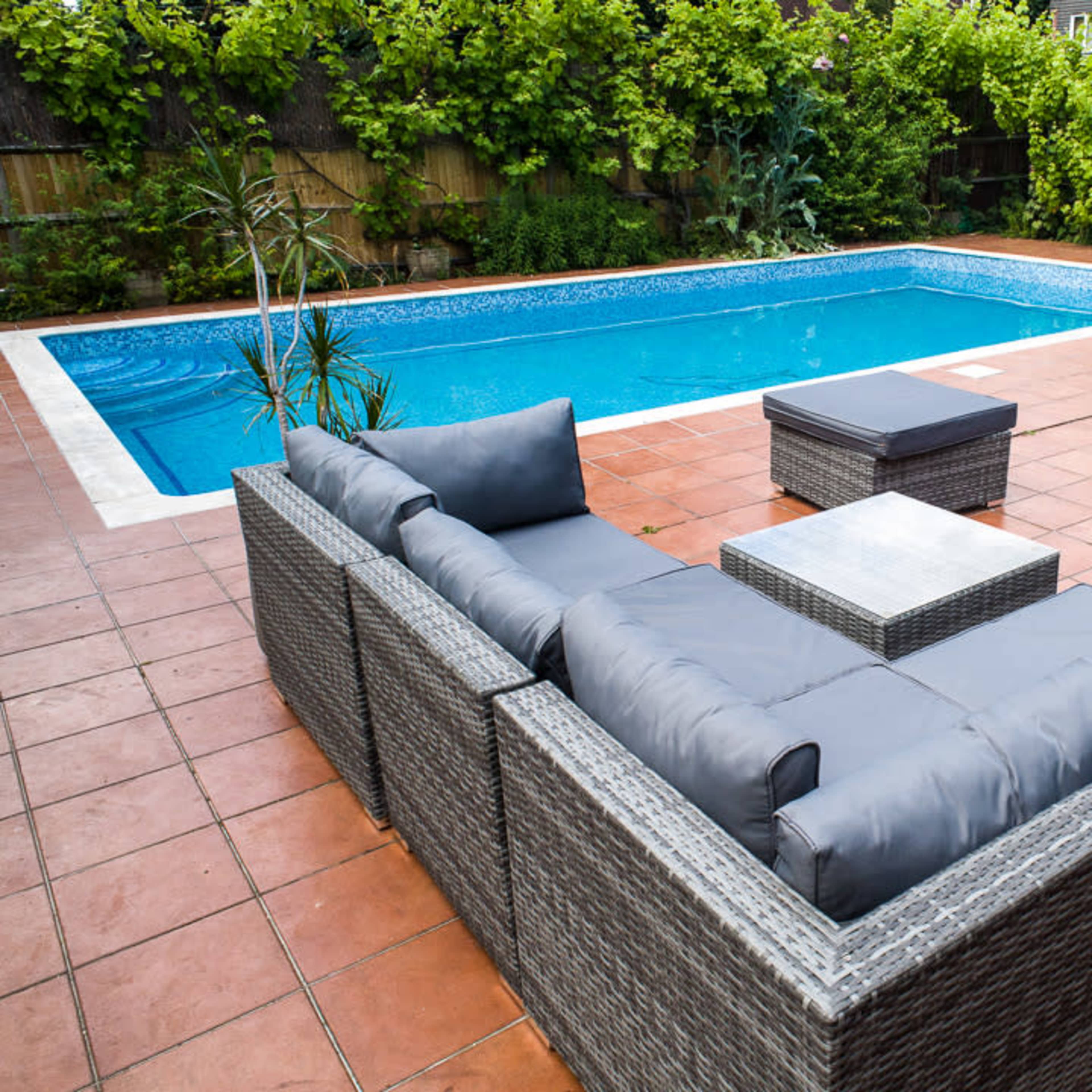 A patio area with a rectangular swimming pool surrounded by tile flooring and a seating arrangement made of outdoor furniture.