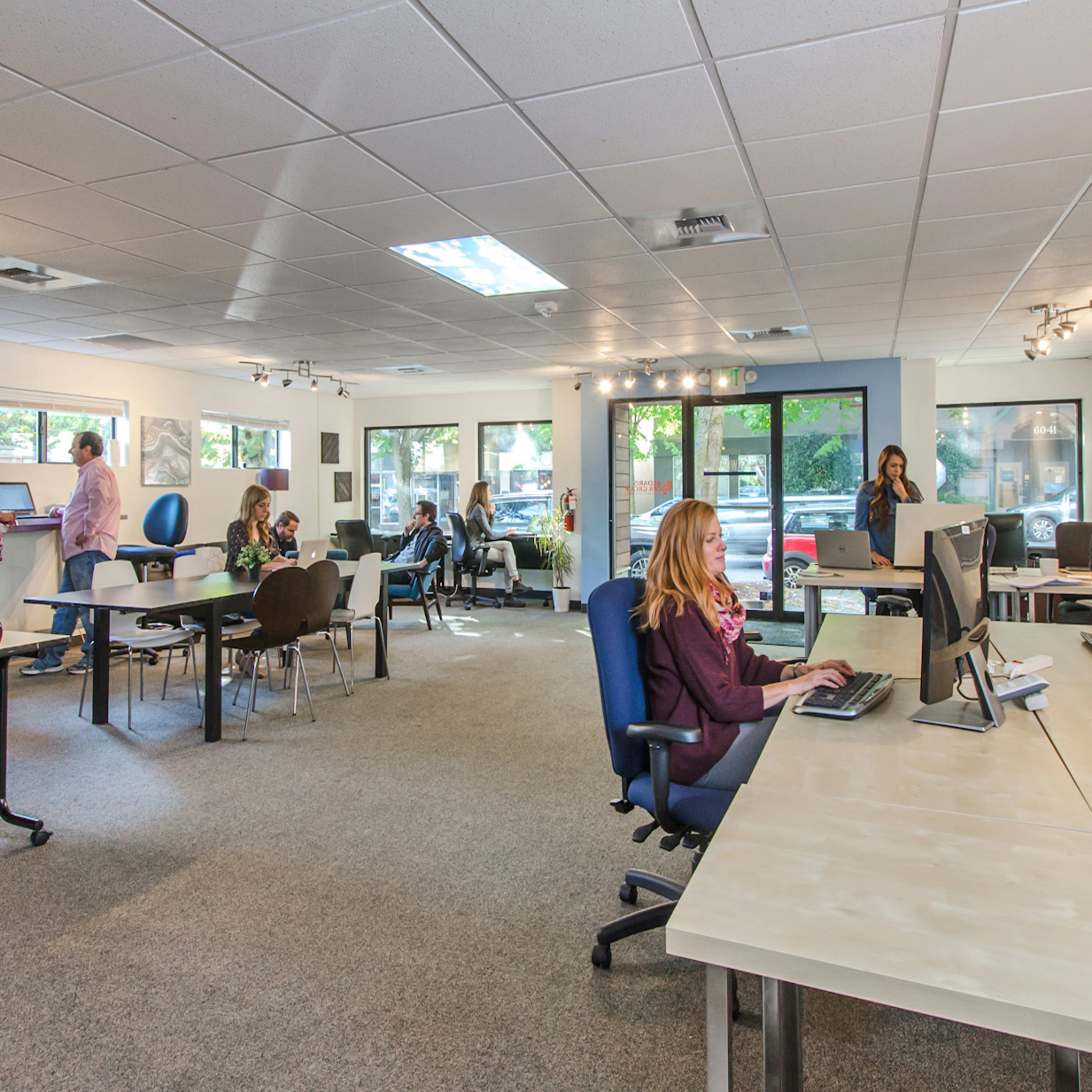An office space with several people working at desks and using computers in a well-lit environment.