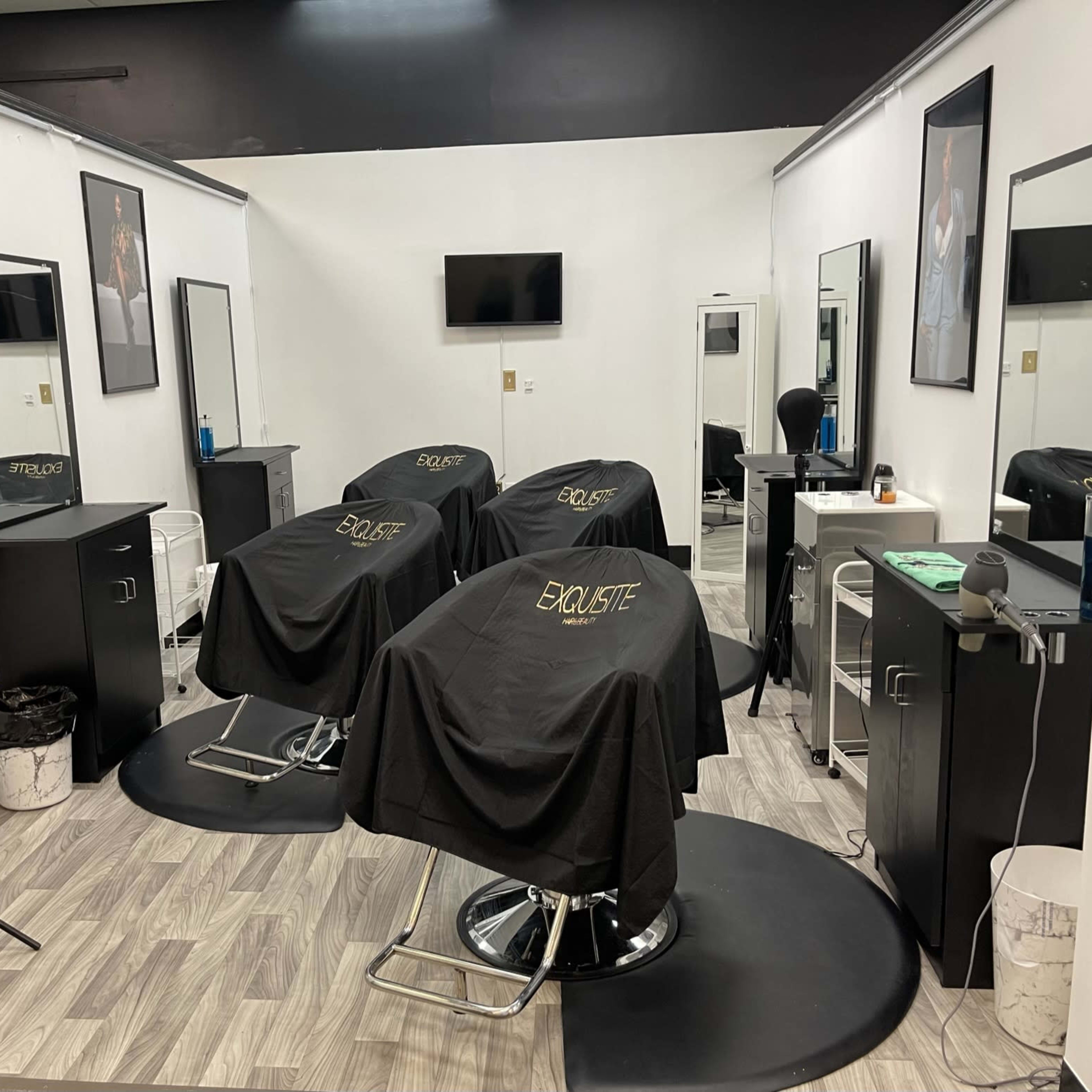 A modern hair salon with three styling chairs, each covered with a black cape, surrounded by mirrors and illuminated by a ring light.