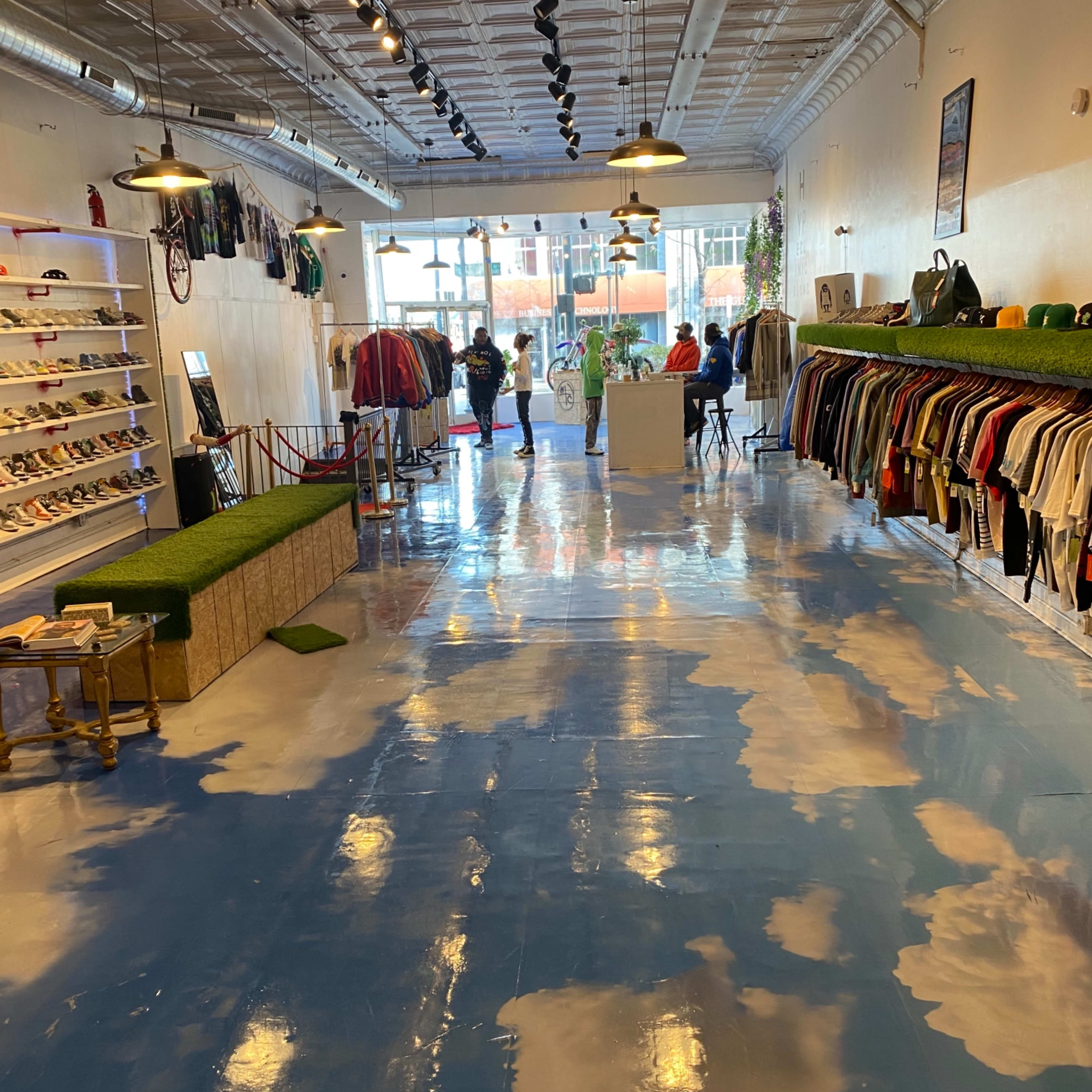 The interior of a retail store features a blue floor painted with cloud patterns, clothing racks along the walls, and customers browsing in the background.