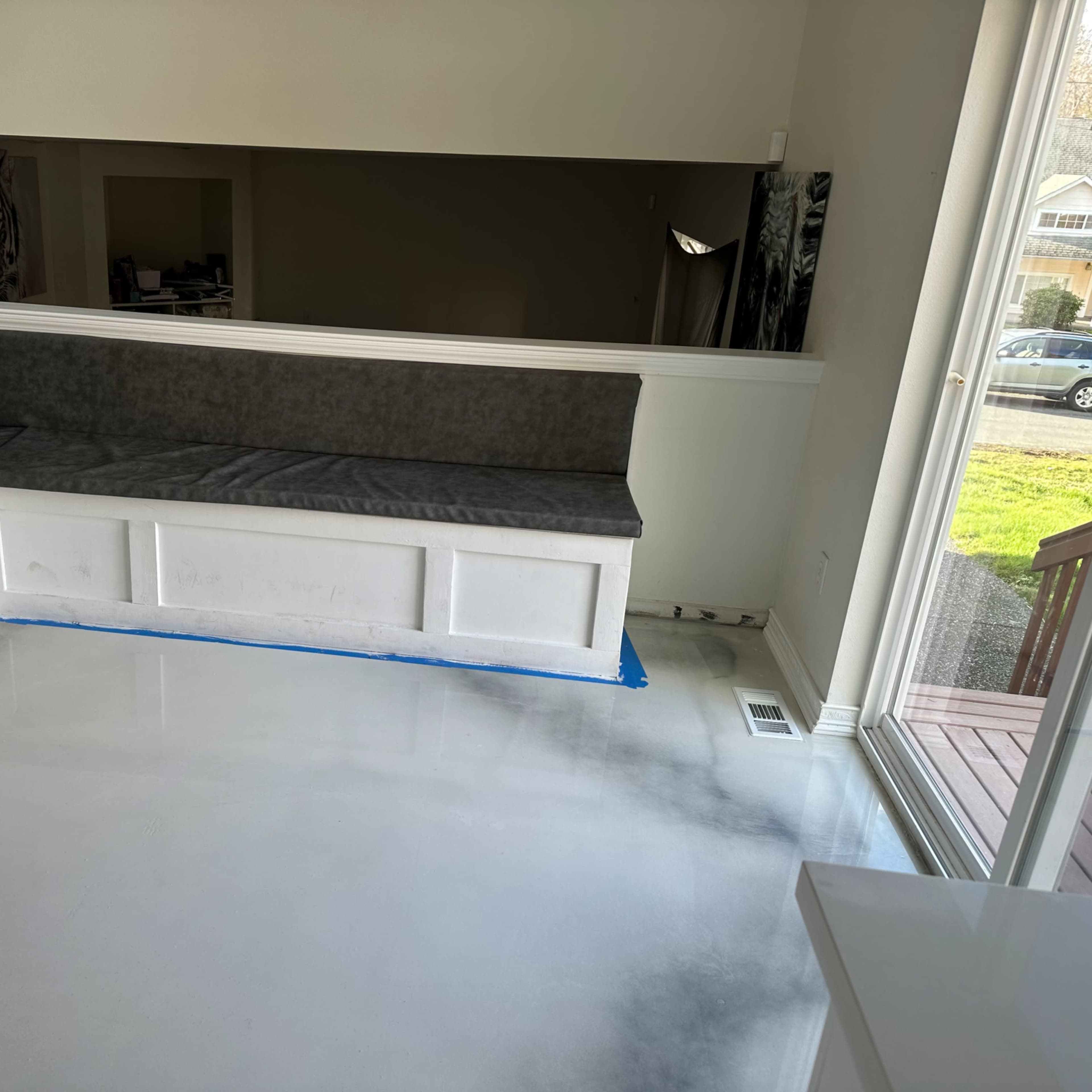 A partially renovated room with a gray cushioned bench built into a white panel along the wall, and a polished concrete floor.