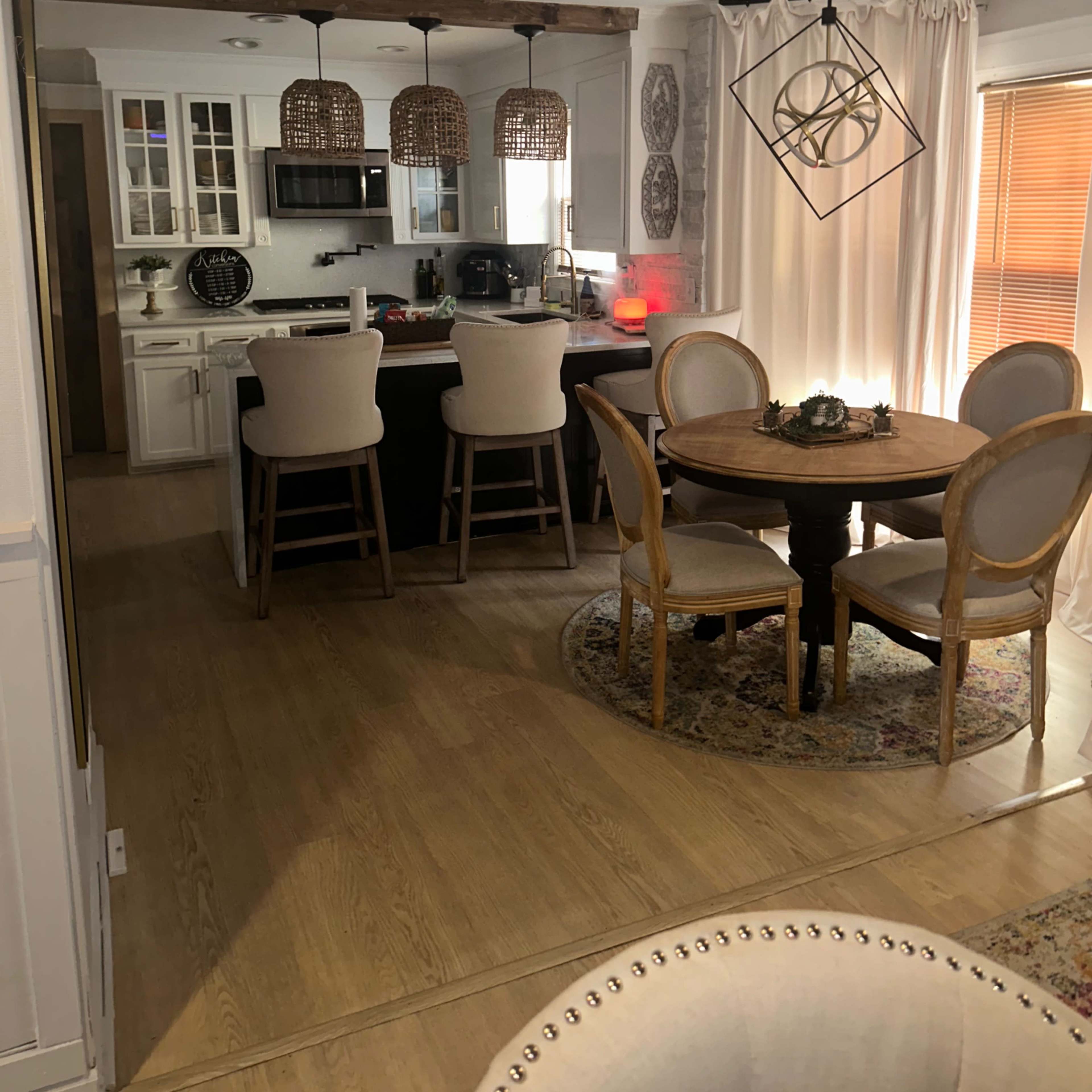 A modern kitchen and dining area with a round table and four chairs, a bar counter with stools, and decorative lighting fixtures.