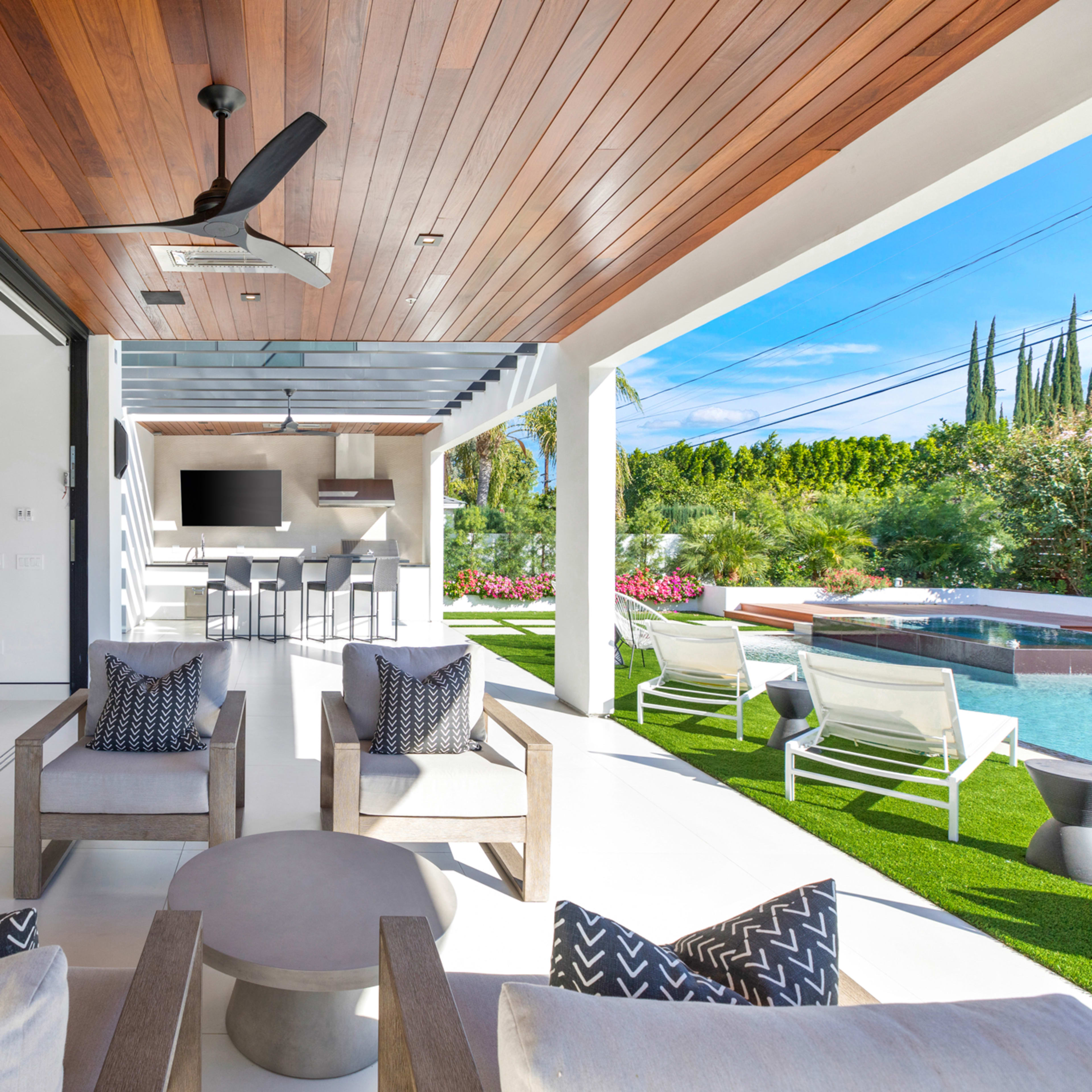 A modern outdoor living space features a seamless transition from a stylish indoor area to a poolside setting with seating and an outdoor kitchen.