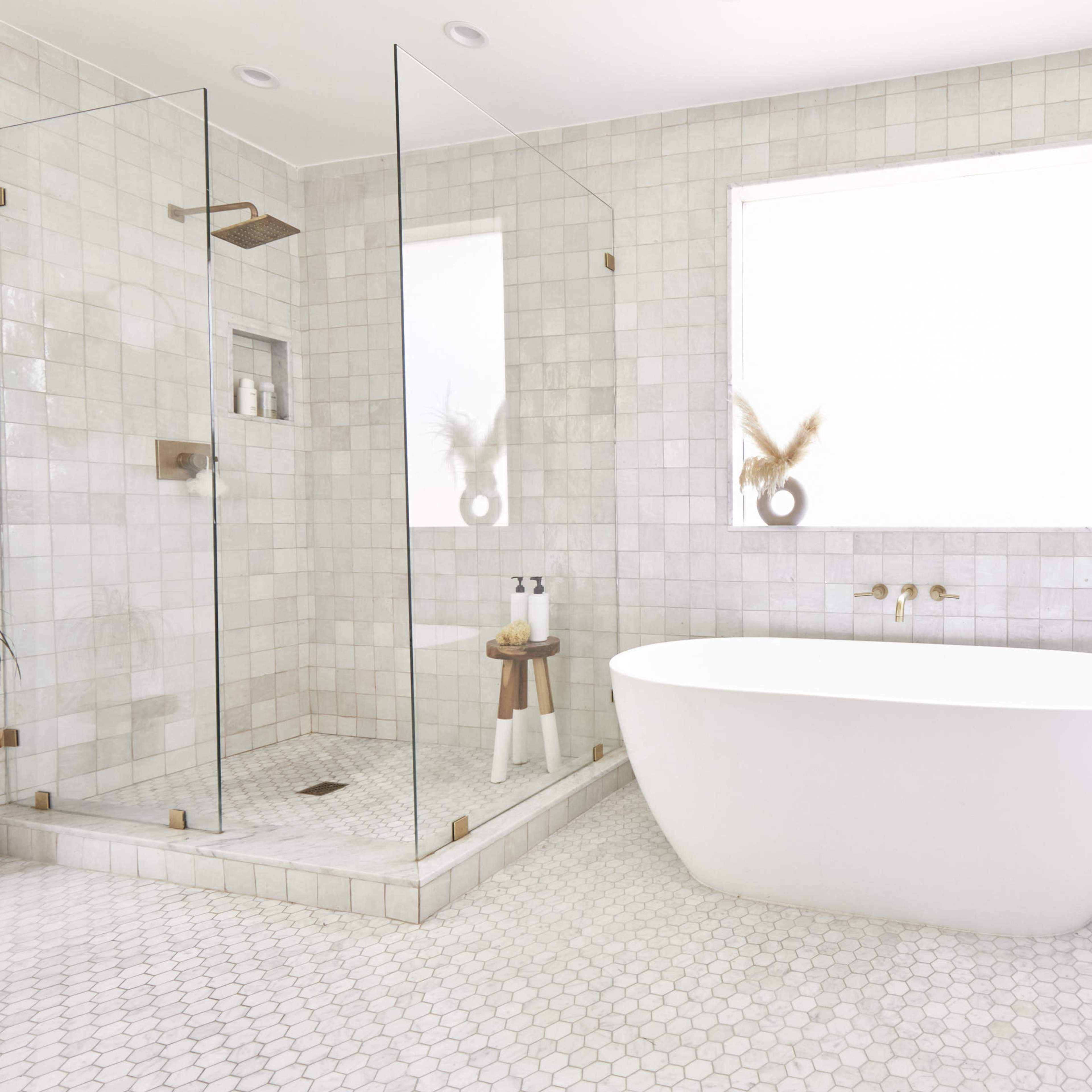 The bathroom features a freestanding white bathtub, a glass shower enclosure, and light-colored tile flooring.