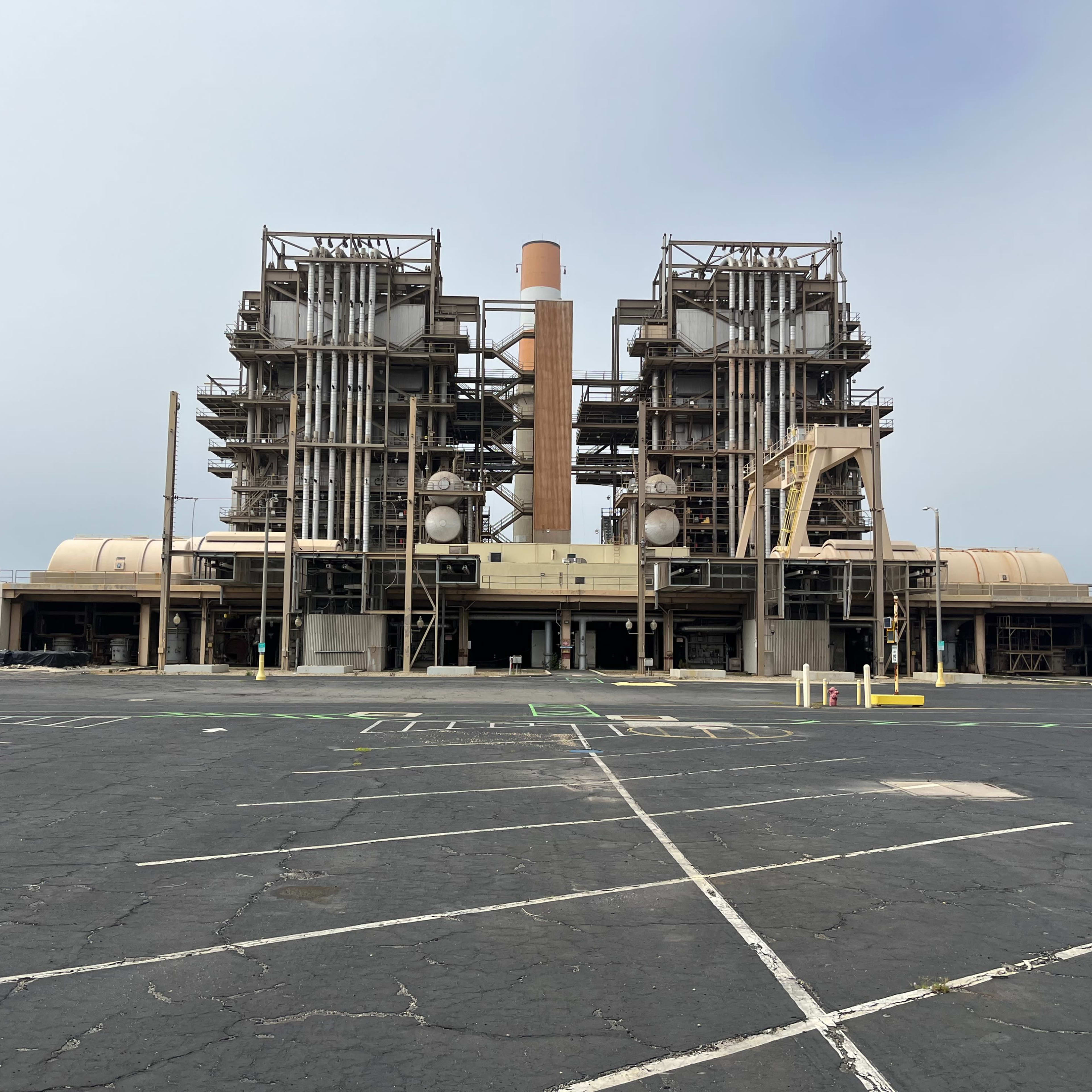 A power plant with large industrial structures and cooling towers, set against a cloudy sky.