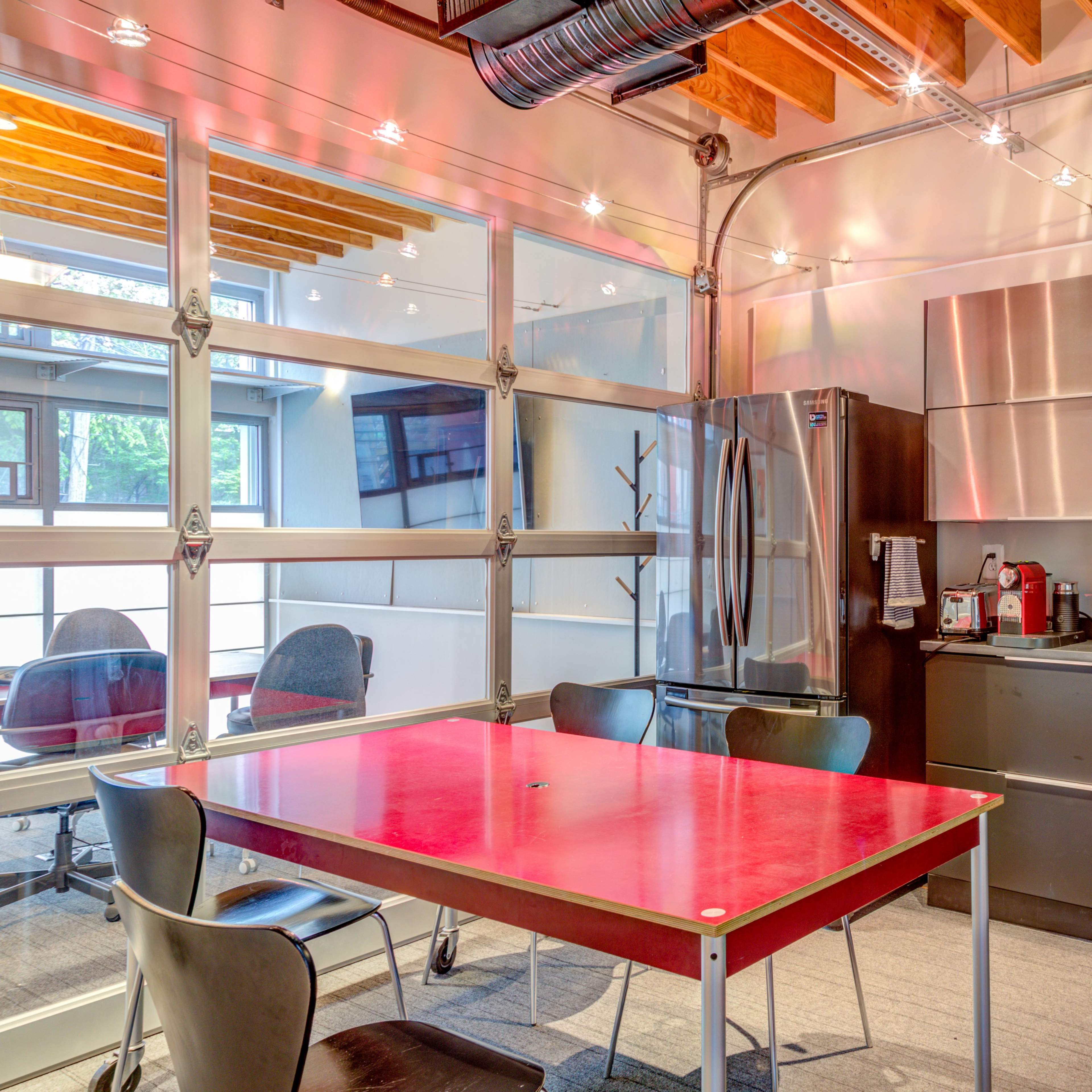 A modern kitchen and dining area with a red table, black cabinetry, stainless steel appliances, and large glass garage doors.