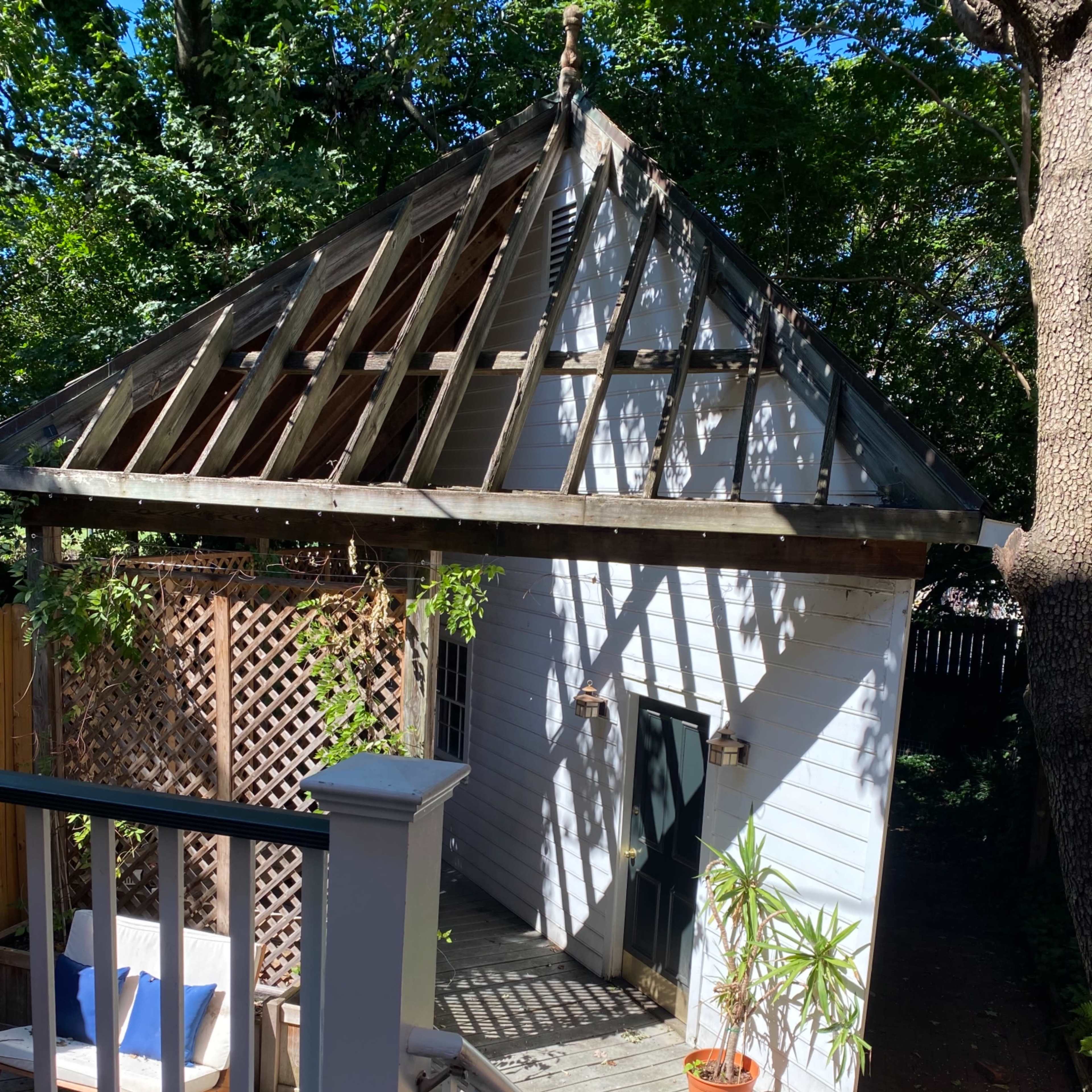 A small, partially constructed building with an open roof sits at the end of a garden path, surrounded by greenery.