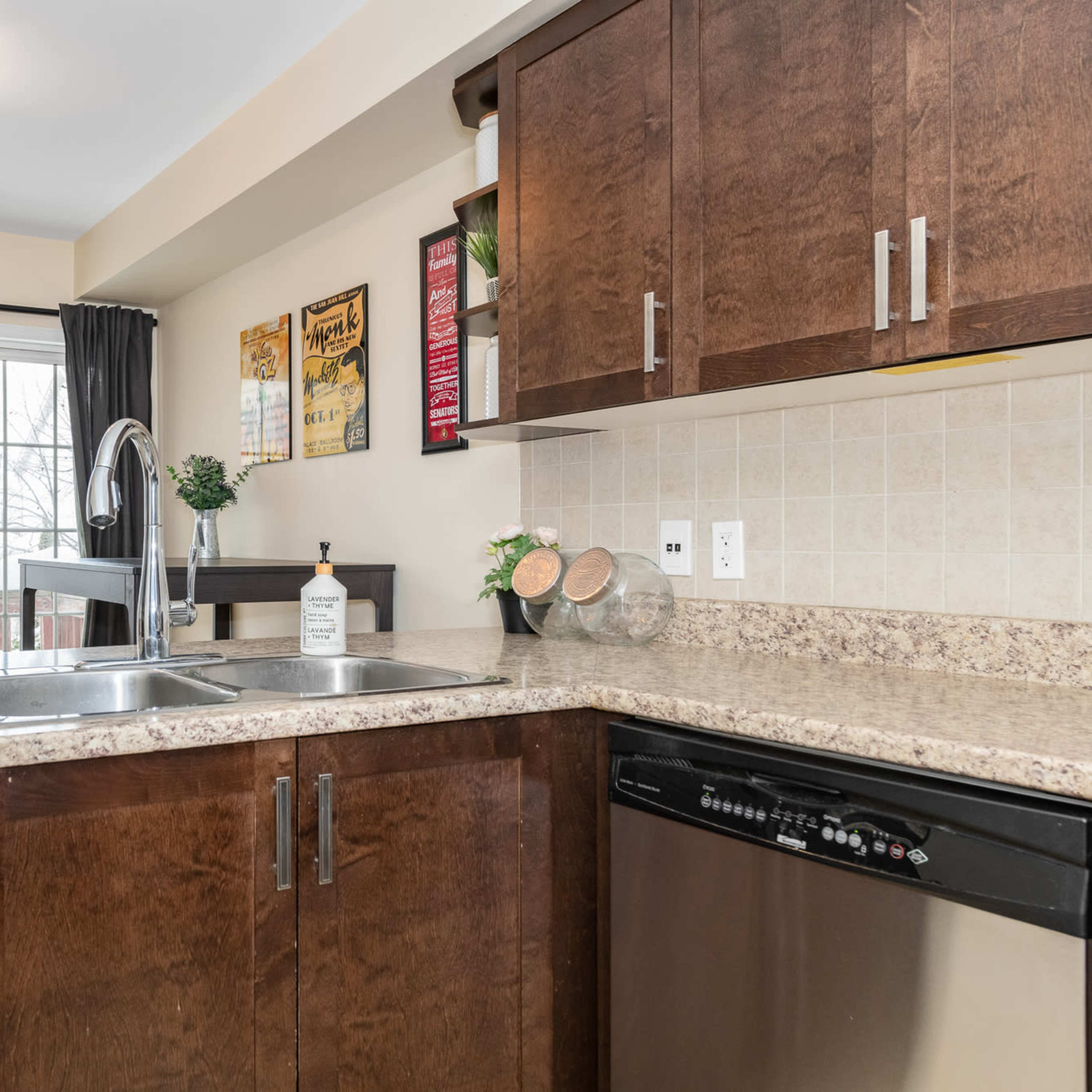 A modern kitchen features wooden cabinetry, a double sink, and a view through a large window with sliding doors to an outdoor space.